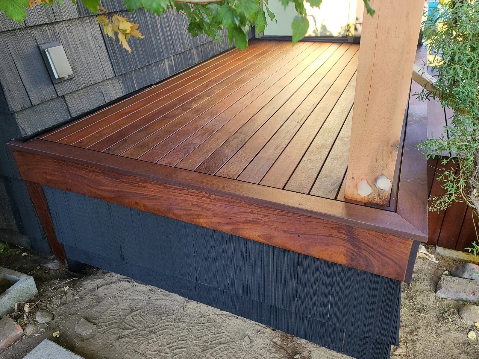 Newly installed wooden deck with wooden posts and surrounding plants outside the house.