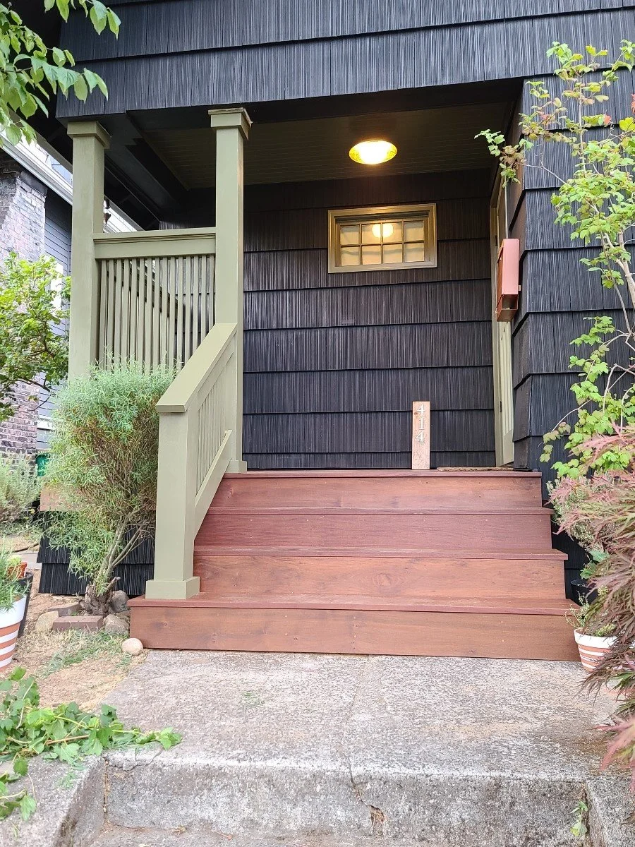 Front porch with wooden stairs, black house siding, small window, light fixture, potted plants, and house number 414