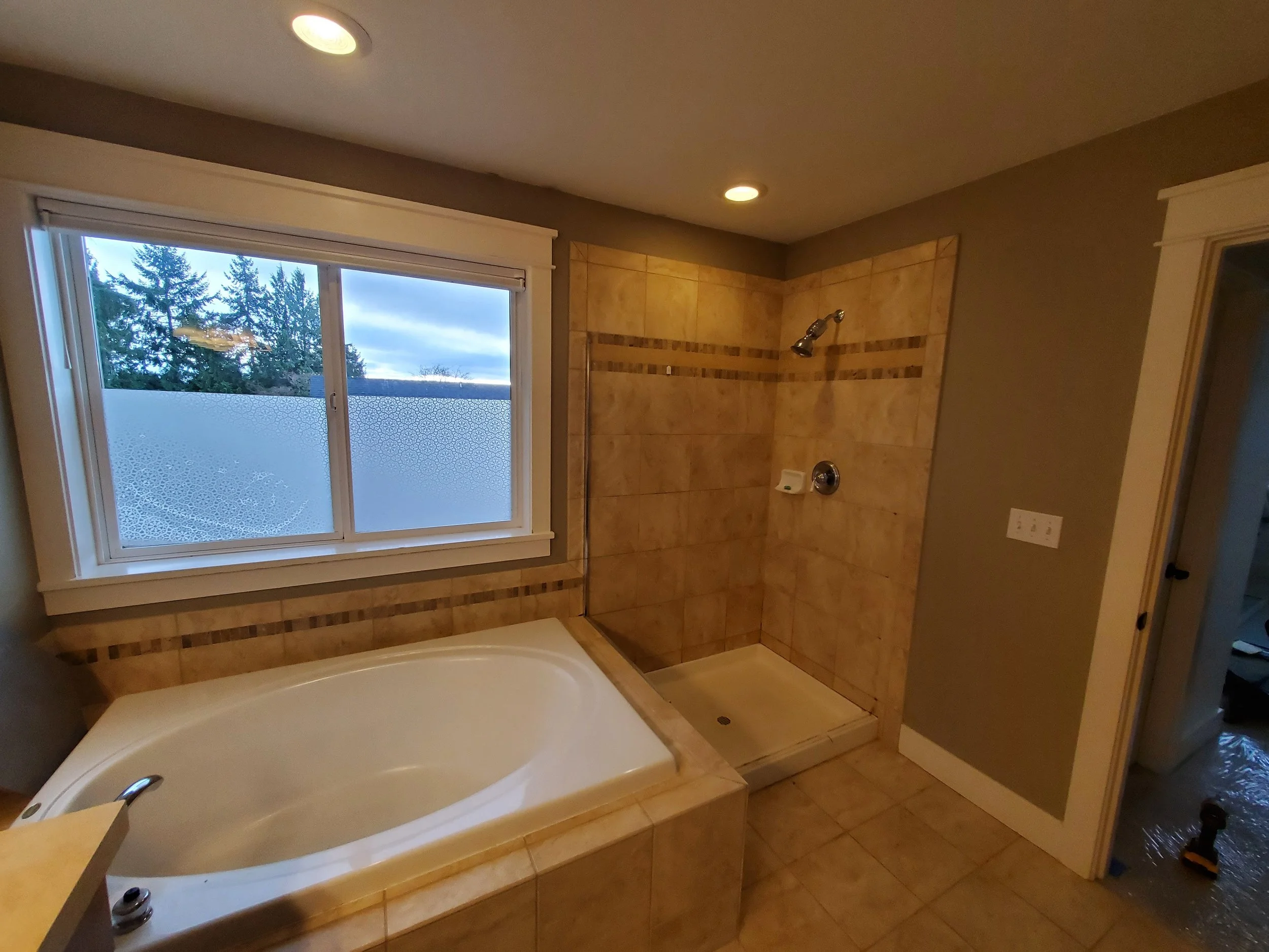 Bathroom with a corner bathtub under a large window and a walk-in shower with beige tiles.