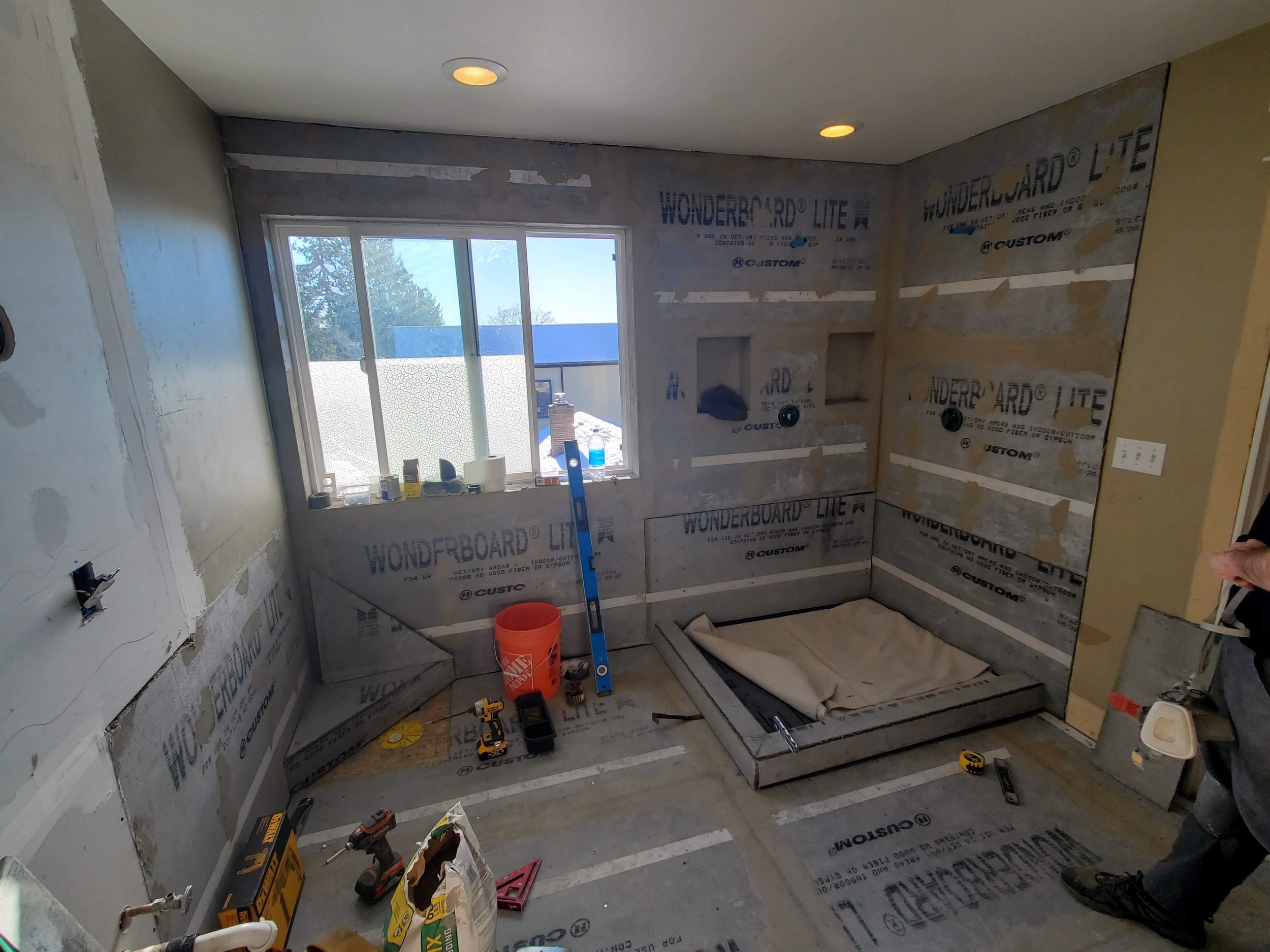 Room under construction with drywall installation in progress, tools on the floor, and a window with sunlight coming in.