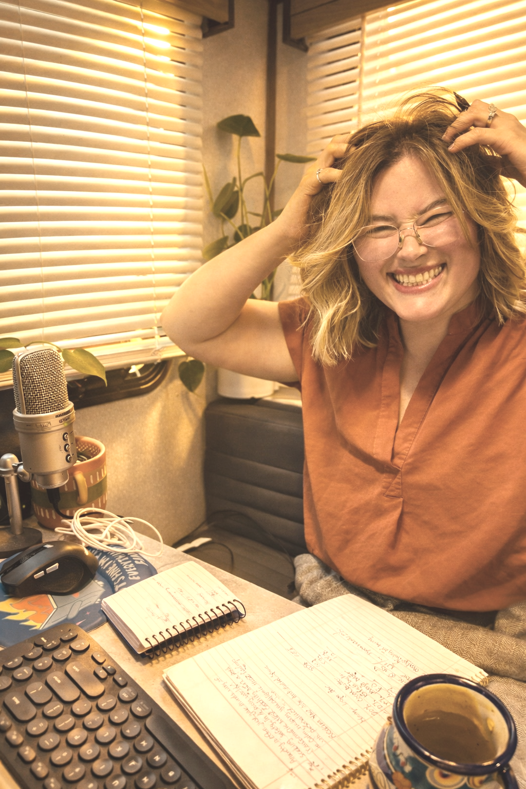 A smiling woman in an orange short-sleeve blouse at a table frizzing her short hair
