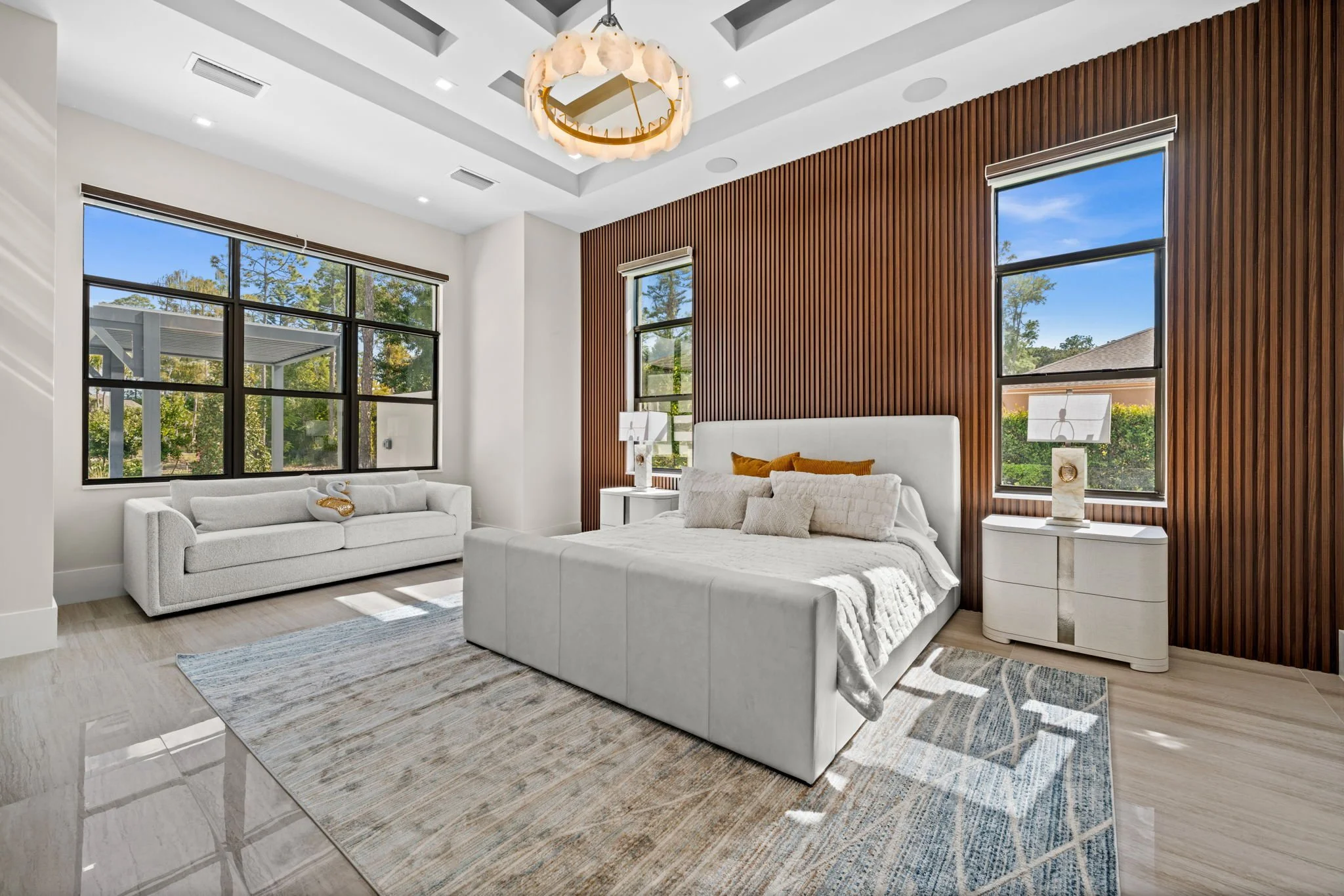 Modern bedroom with white furniture, wooden accent wall, large windows, and a ceiling light fixture
