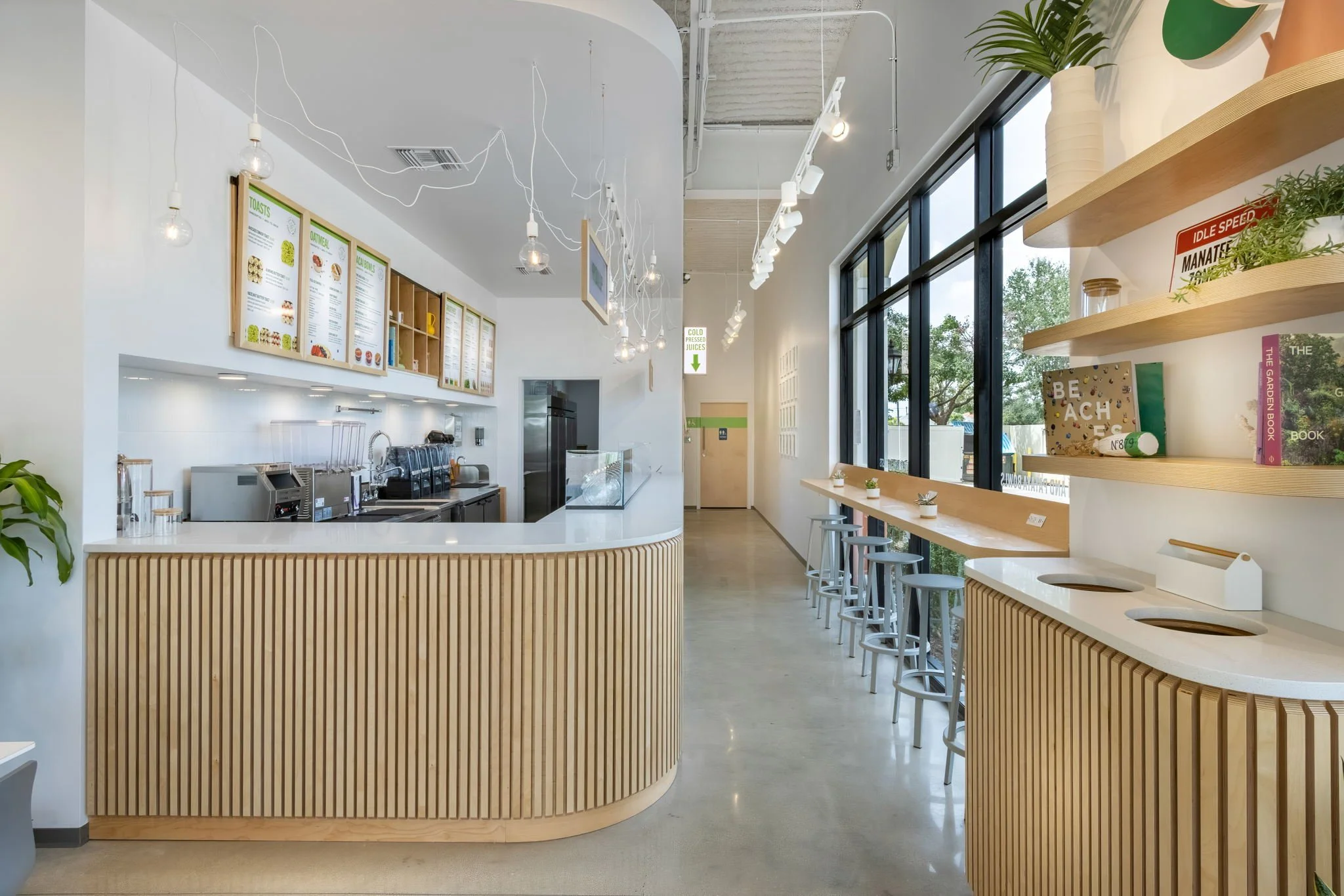 Interior of a modern cafe with light wood accents, hanging light bulbs, a counter with equipment, and large windows letting in natural light.