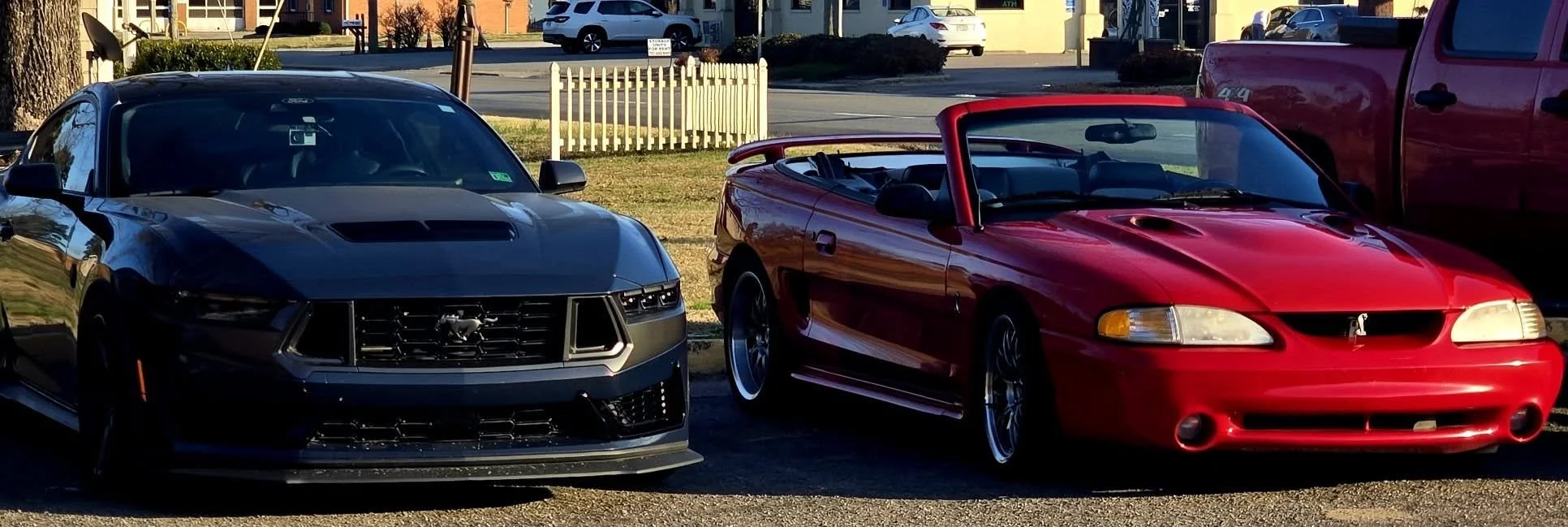 Blue Ember Metallic Ford Mustang Dark Horse and red Ford Mustang Cobra in a parking lot during daytime.