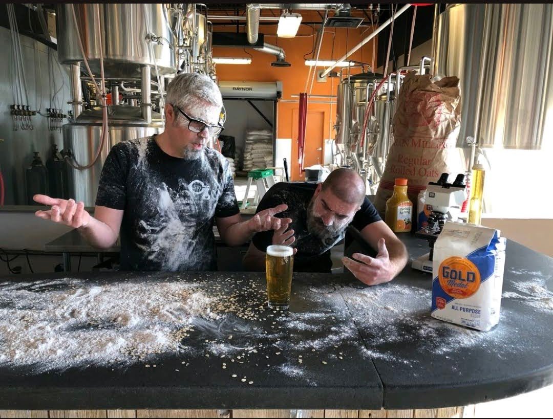 404 Page: Brewery Owners comically covered in flour looking at a clear beer confused it isn't hazy.