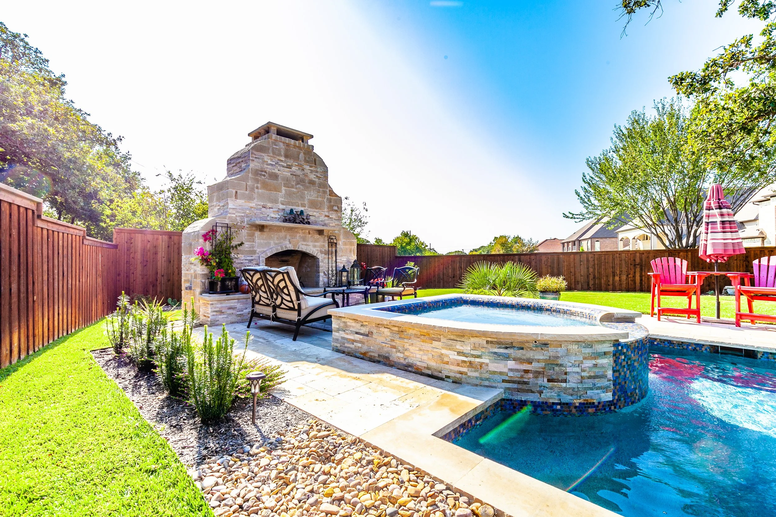 Backyard with a swimming pool, fireplace, patio furniture, and a wooden fence under a clear sky.