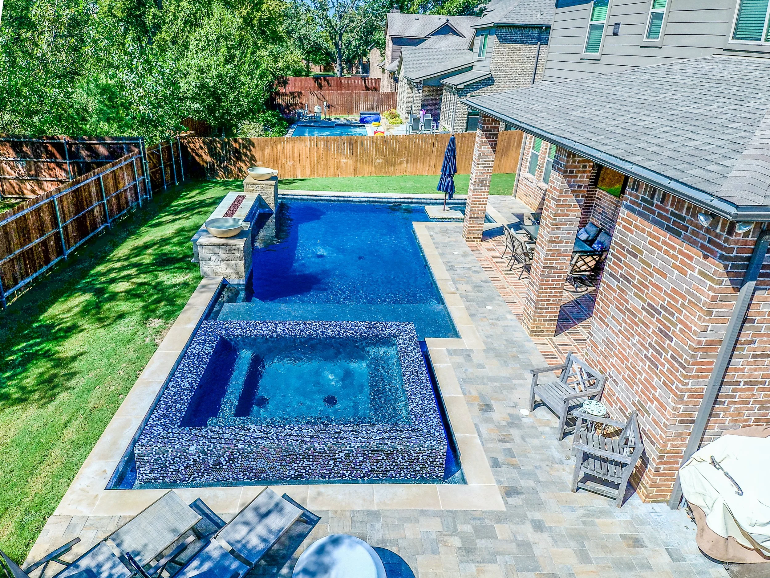 Backyard with swimming pool, hot tub, patio furniture, and a covered porch area with brick columns and a brick house.