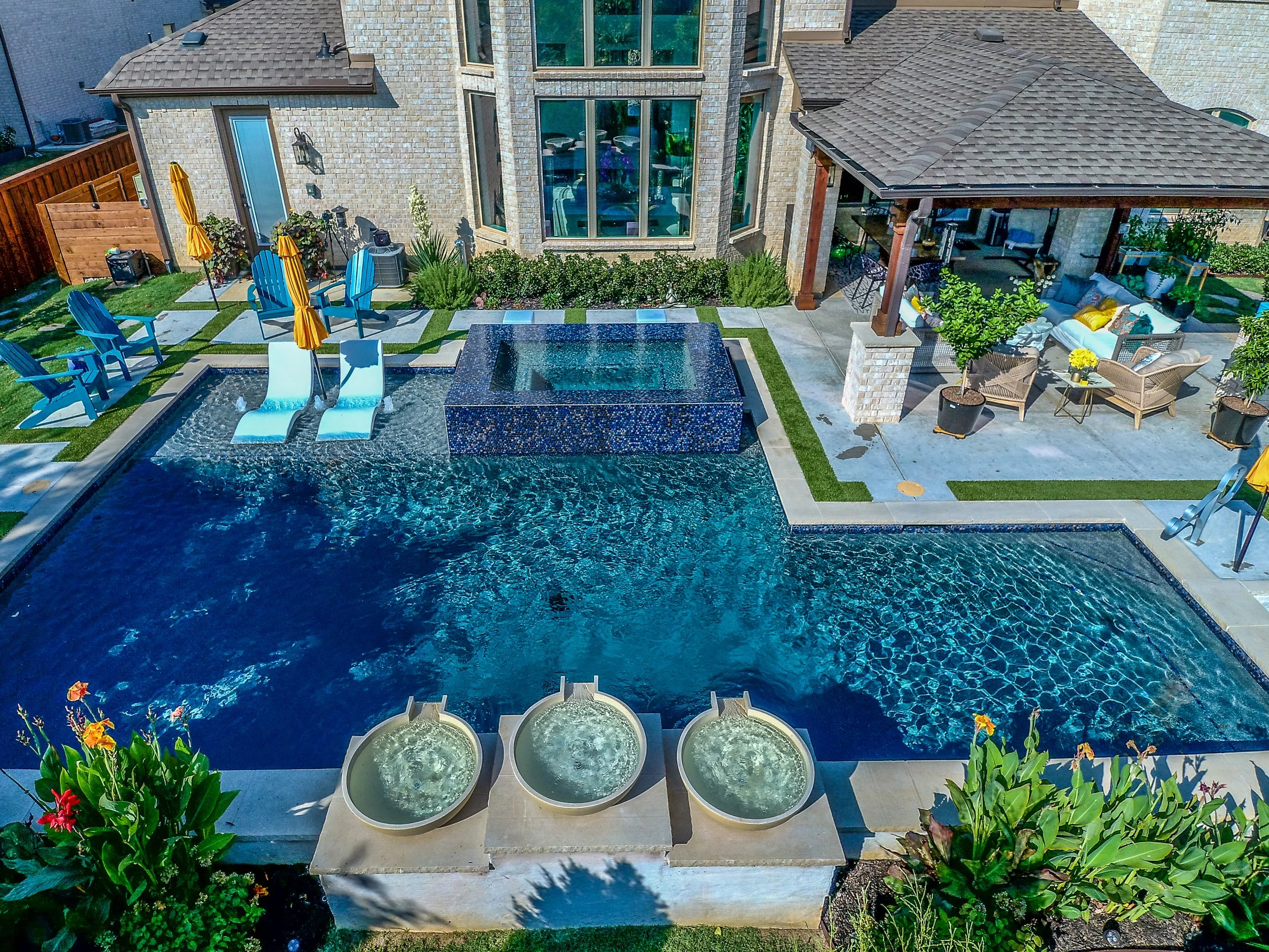 A backyard with a swimming pool, lounge chairs, umbrellas, and outdoor seating area.