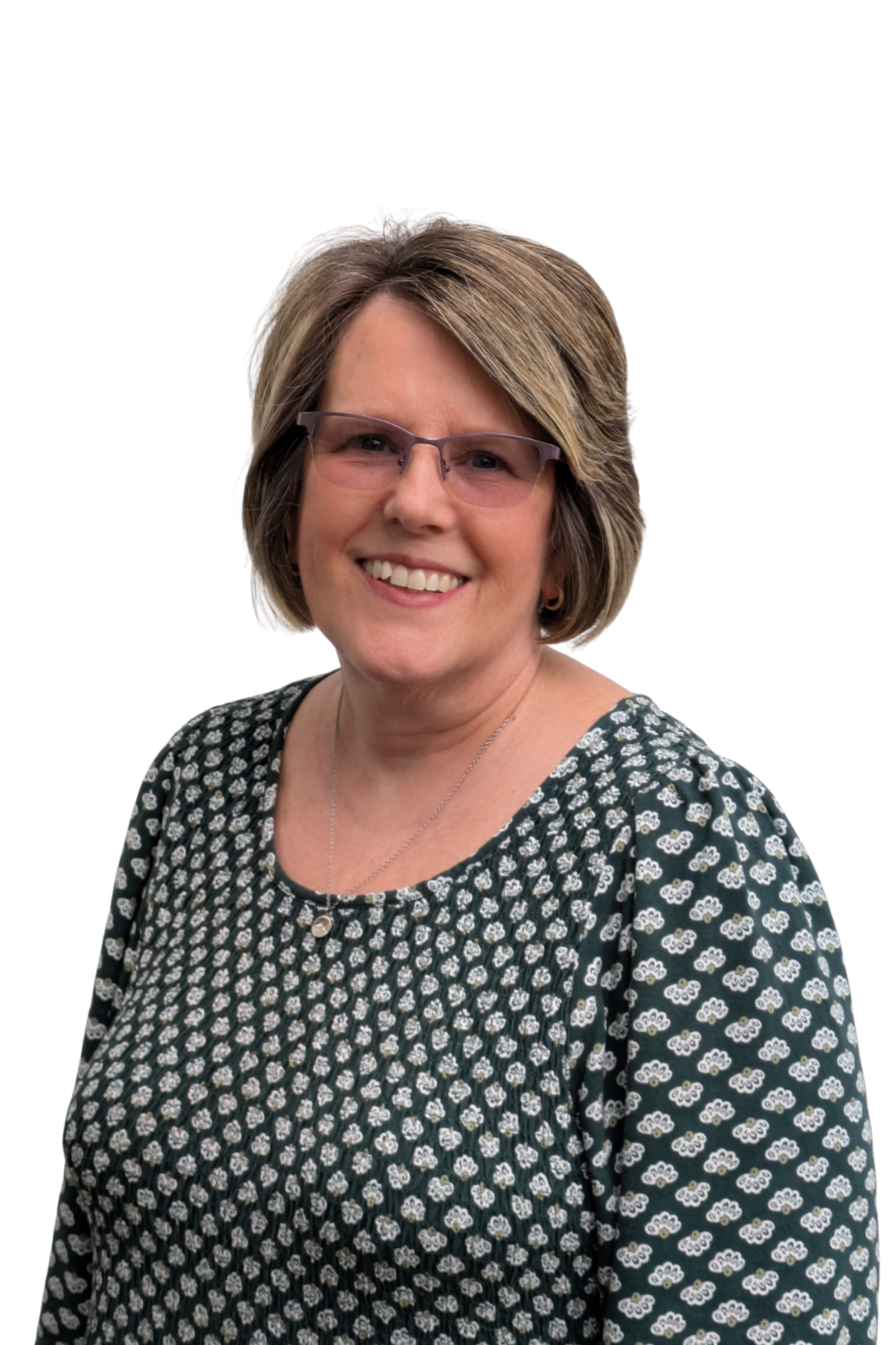 A middle-aged woman with short, layered, light brown hair, wearing glasses with a purple tint, a patterned black and white dress with a small floral design, a necklace, and earrings, smiling in front of a plain white background.