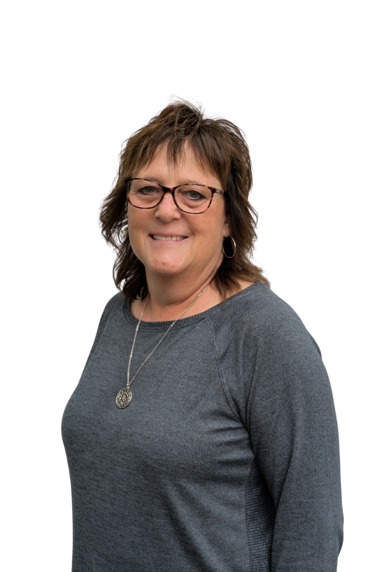 A woman with short brown hair, glasses, and hoop earrings, smiling, wearing a dark grey sweater with a silver necklace, against a plain white background.