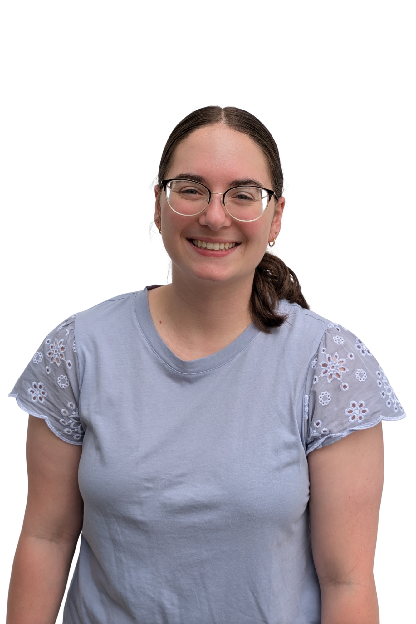 A young woman with brown hair in a ponytail, wearing glasses, gold earrings, and a light blue blouse with eyelet lace sleeves, smiling at the camera, against a plain white background.