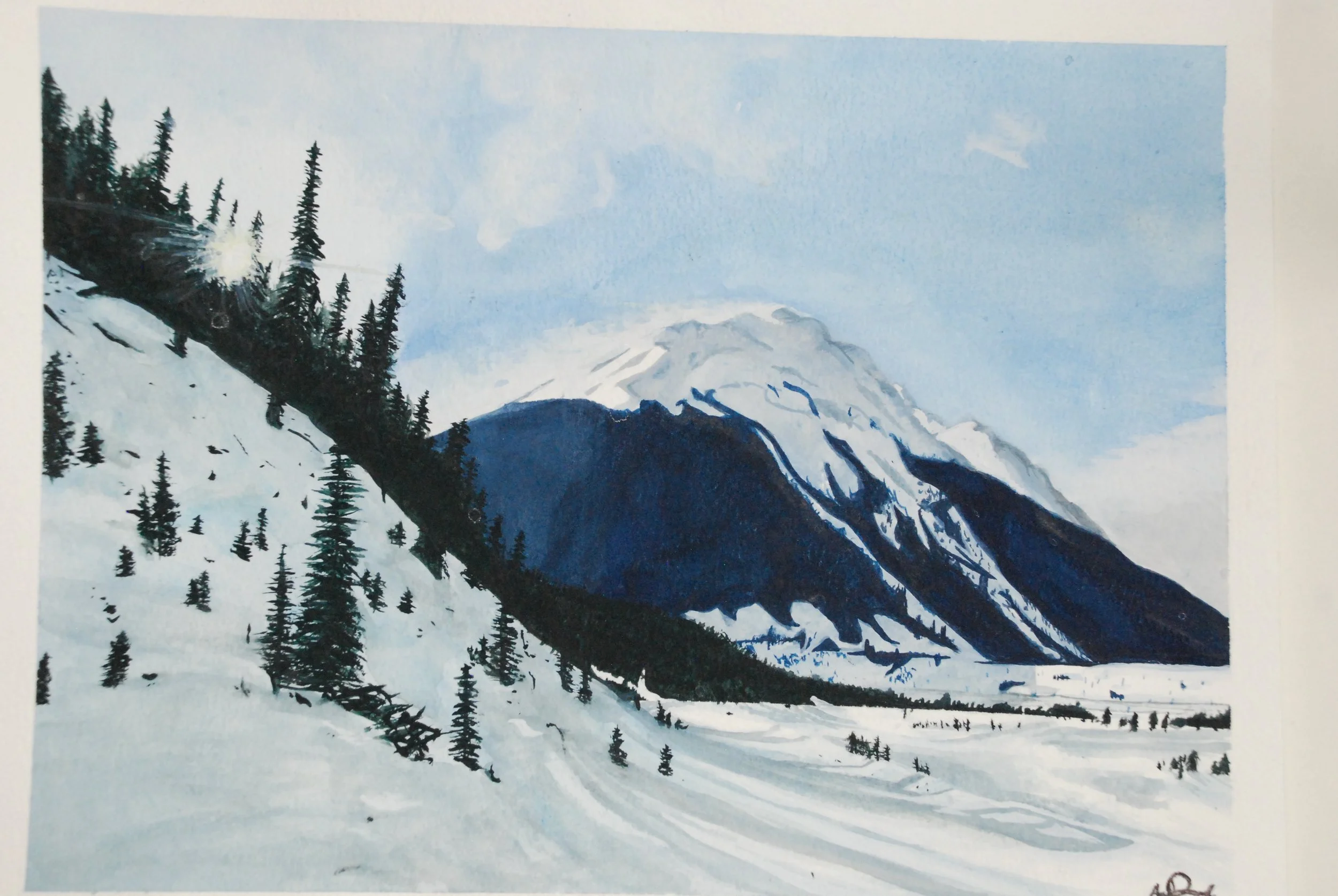 A snow-covered mountain landscape with a large mountain in the background, evergreen trees on a hillside to the left, and a snowfield in the foreground under a partly cloudy sky.