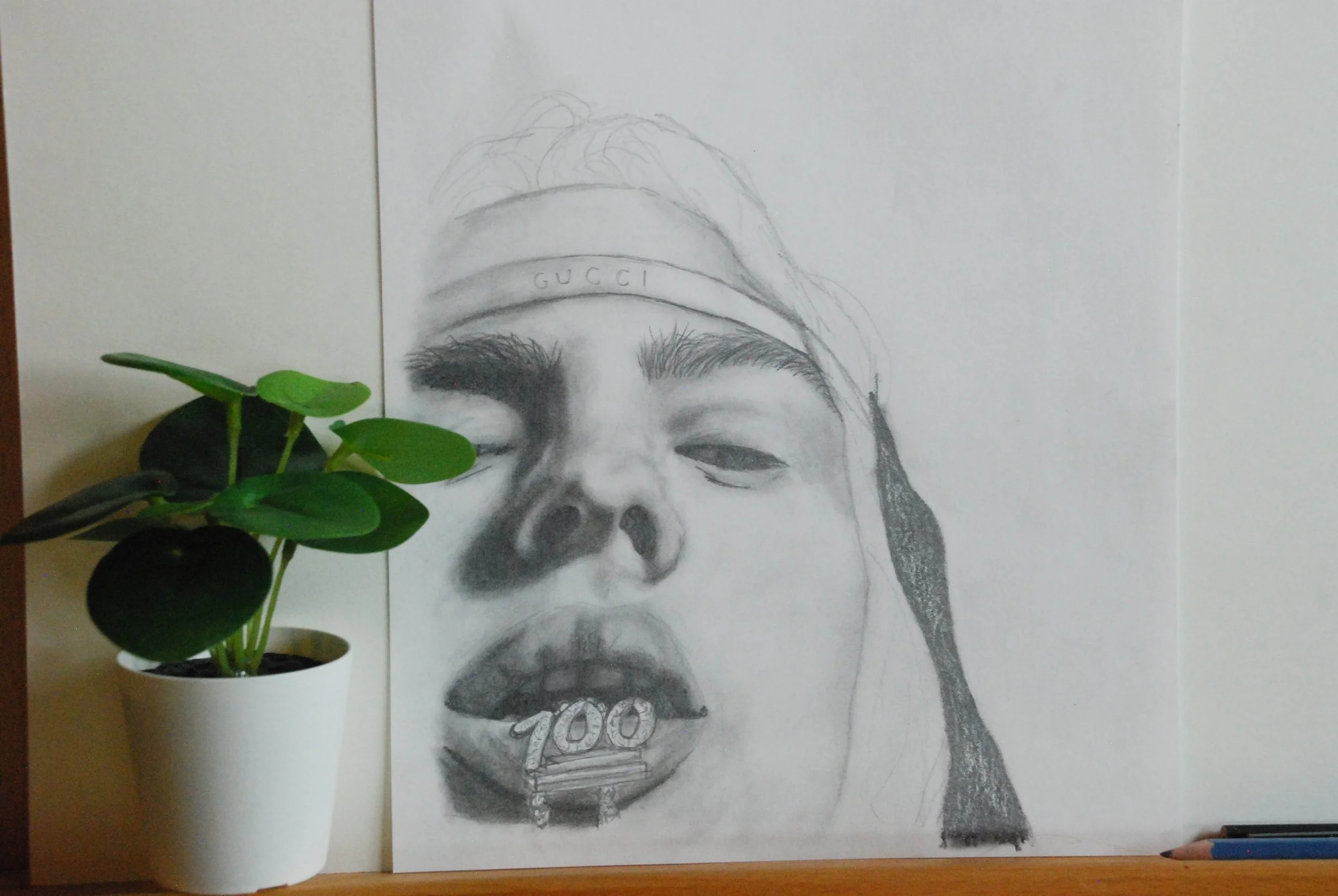 A pencil drawing of a person's face, wearing a Gucci headband, with a potted plant next to it. The person has curly hair, one eye partially closed, and a large mouth with a '100' necklace tucked inside.