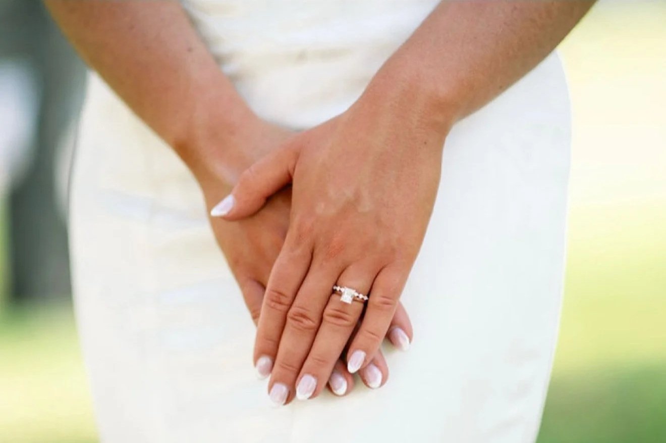 Close-up of a bride's hands with a wedding ring, resting on her white wedding dress.