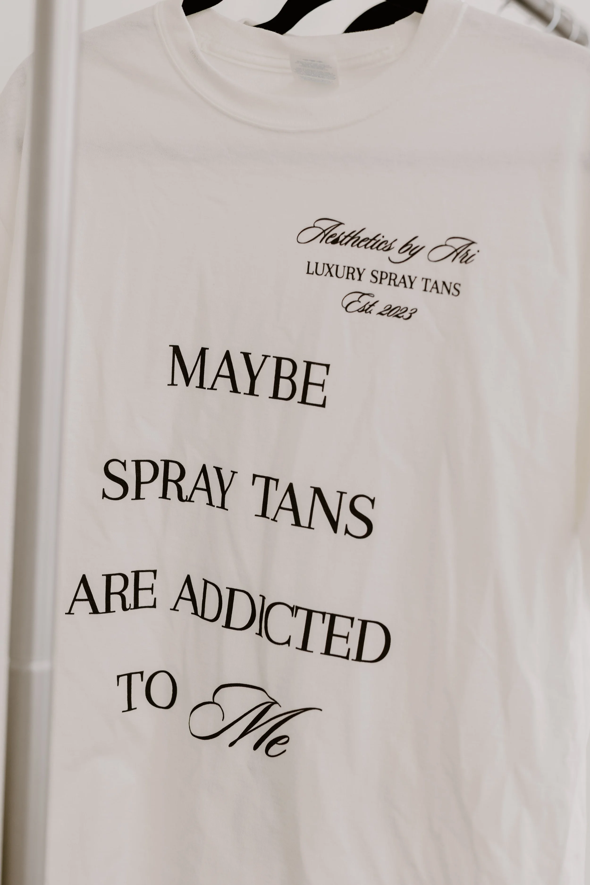 White T-shirt with black text and decorative design hanging on a hanger.