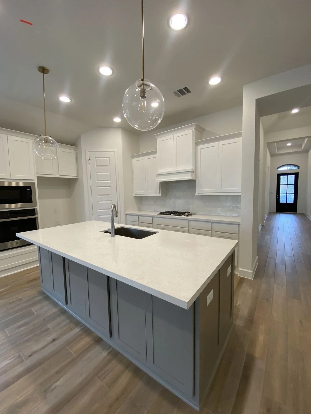 Modern white kitchen with island, pendant lights, hardwood floors, and white cabinetry.