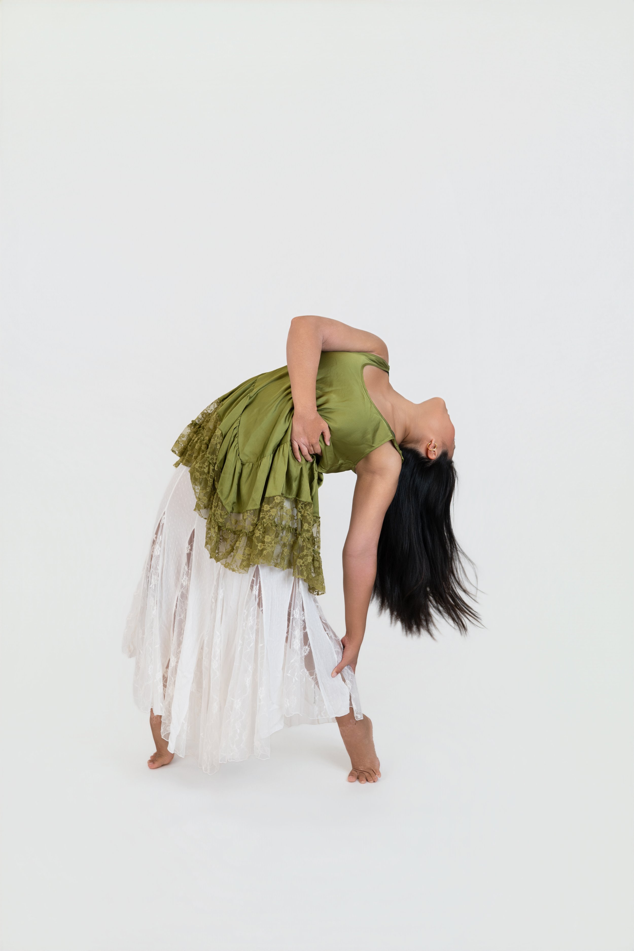 A person practicing ballet in a studio, standing on one leg with the other leg bent and foot resting against the standing leg, wearing ballet slippers, leg warmers, and athletic clothing.