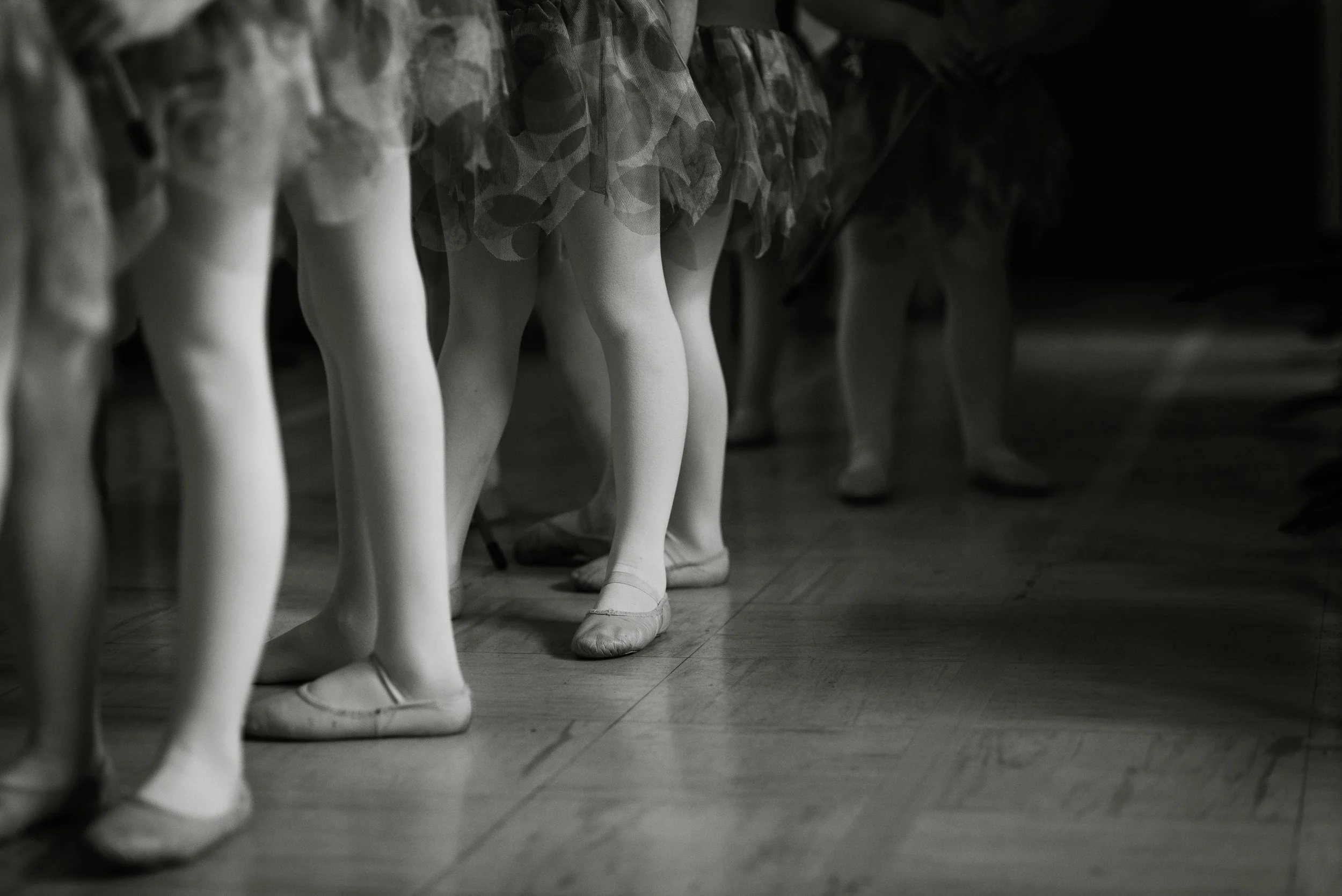 Row of ballet dancer mannequins in tutus and pointe shoes, lined up on a wooden floor.
