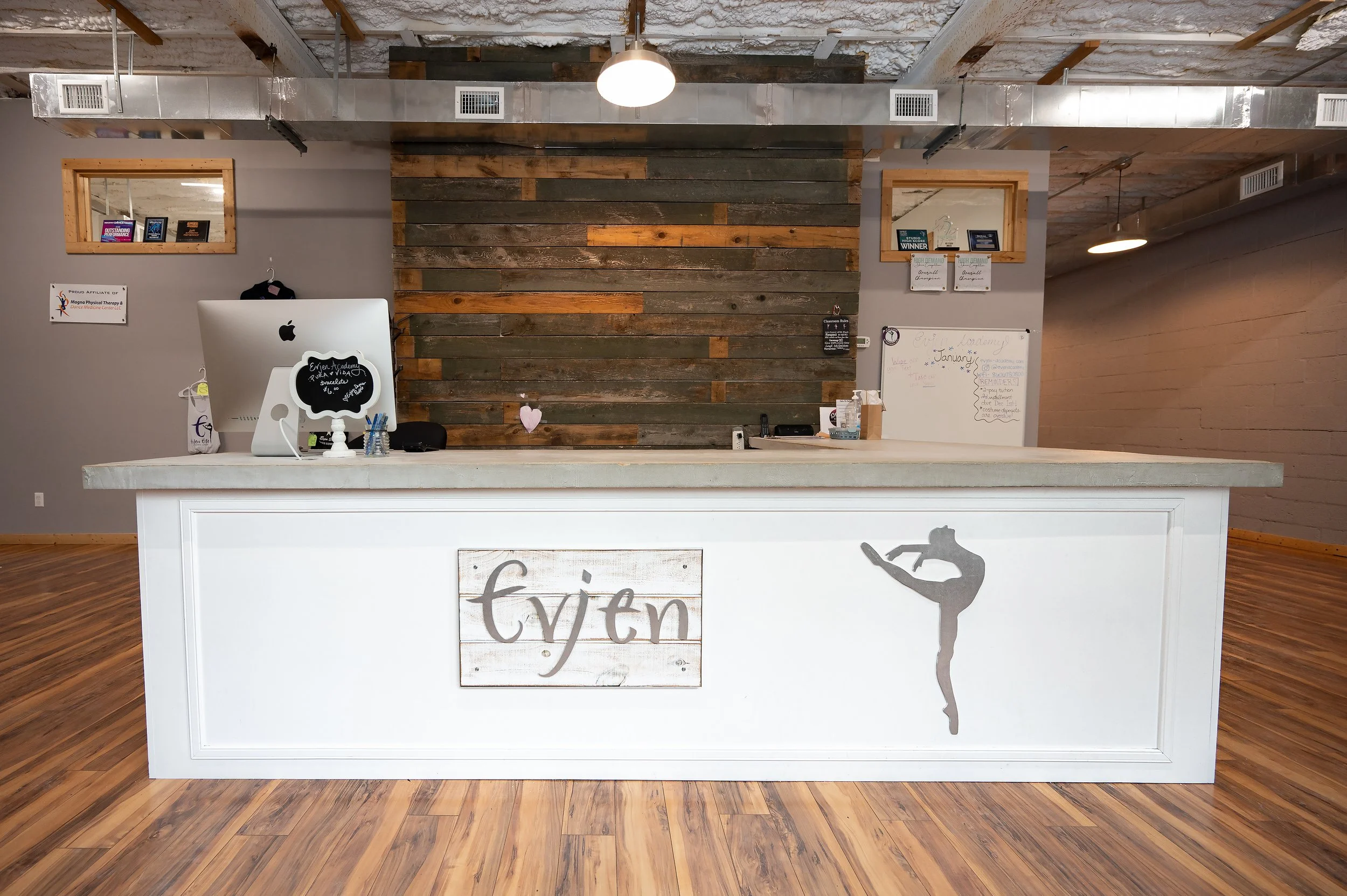 Reception desk with a sign reading 'fytin' in front, a rustic wood wall behind, and framed items on the wall to the sides, in a modern interior space.