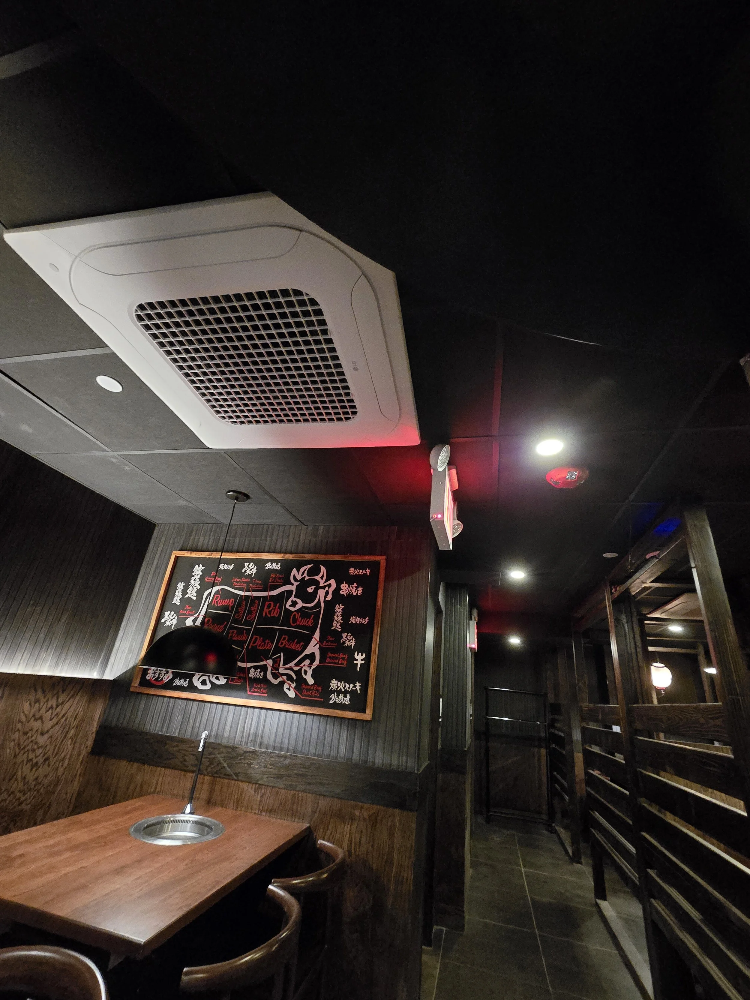 Interior of a restaurant with a black ceiling, wooden walls, a table with a small lamp, a blackboard with a cow diagram and labels, and dim lighting.