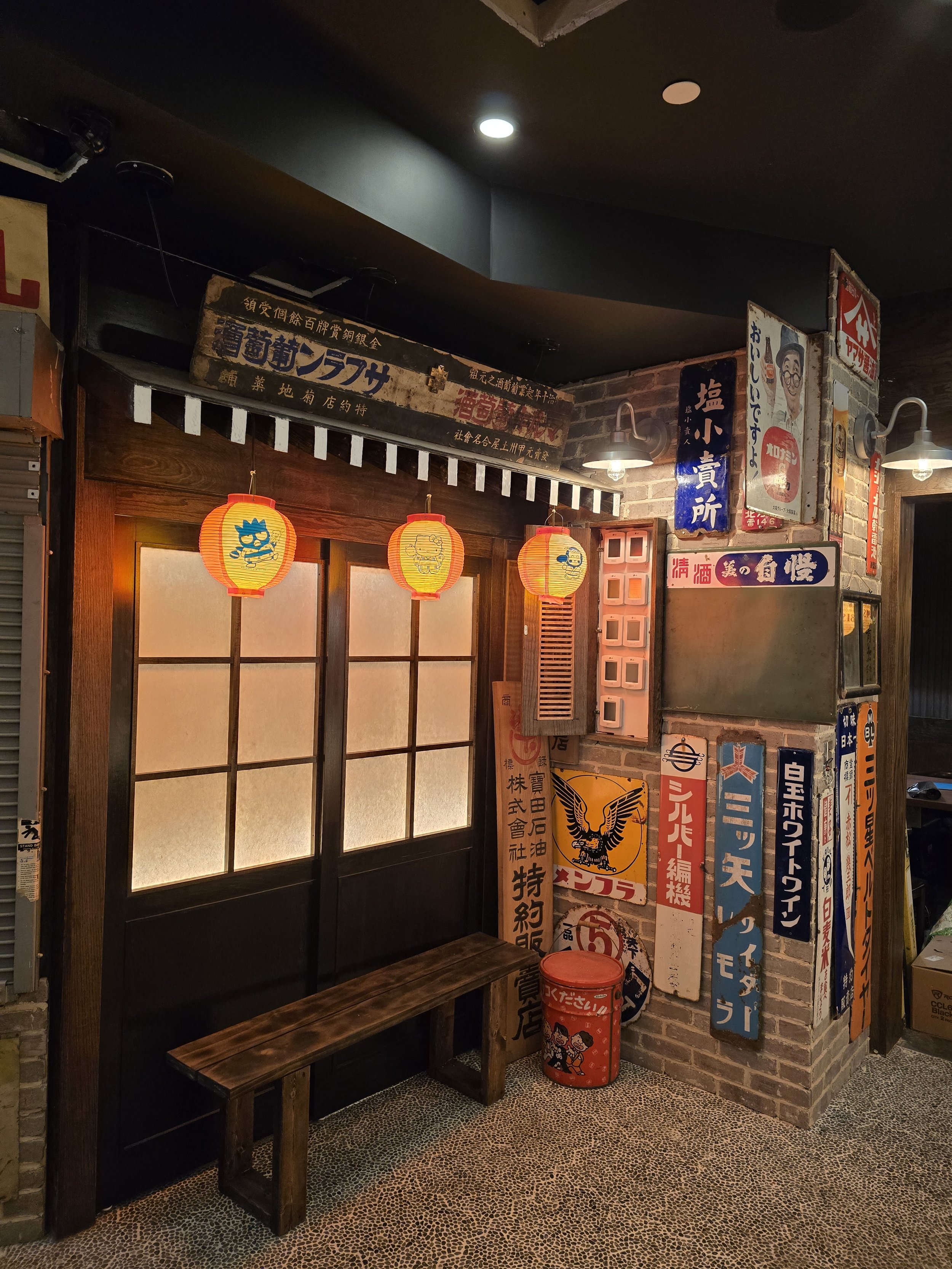 Decorative Japanese-style entrance with paper lanterns, wooden sliding doors, vintage signs, and a small wooden bench.