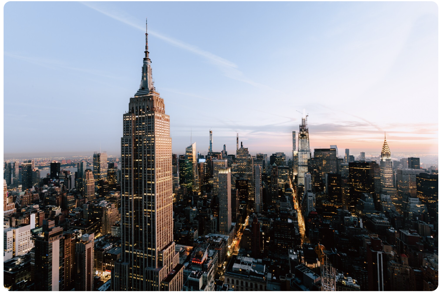 Aerial view of New York City skyline at sunset, featuring the Empire State Building in the foreground and various skyscrapers in Manhattan.