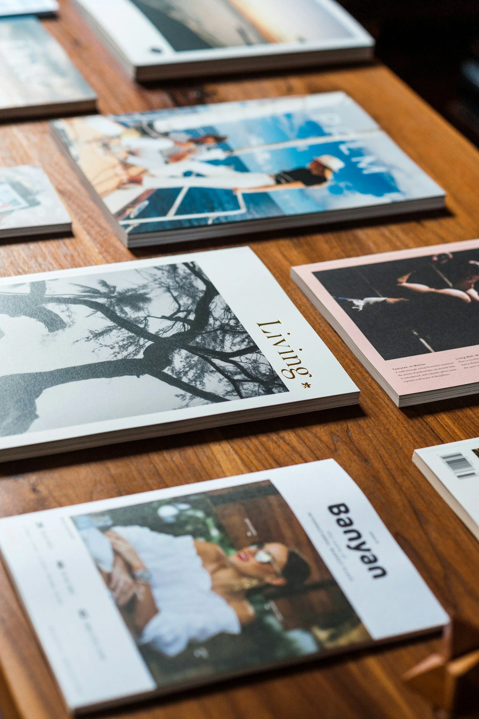 Several magazines with various covers laid out on a wooden table, including one with a black and white photo of a tree and the word 'living' on the cover.