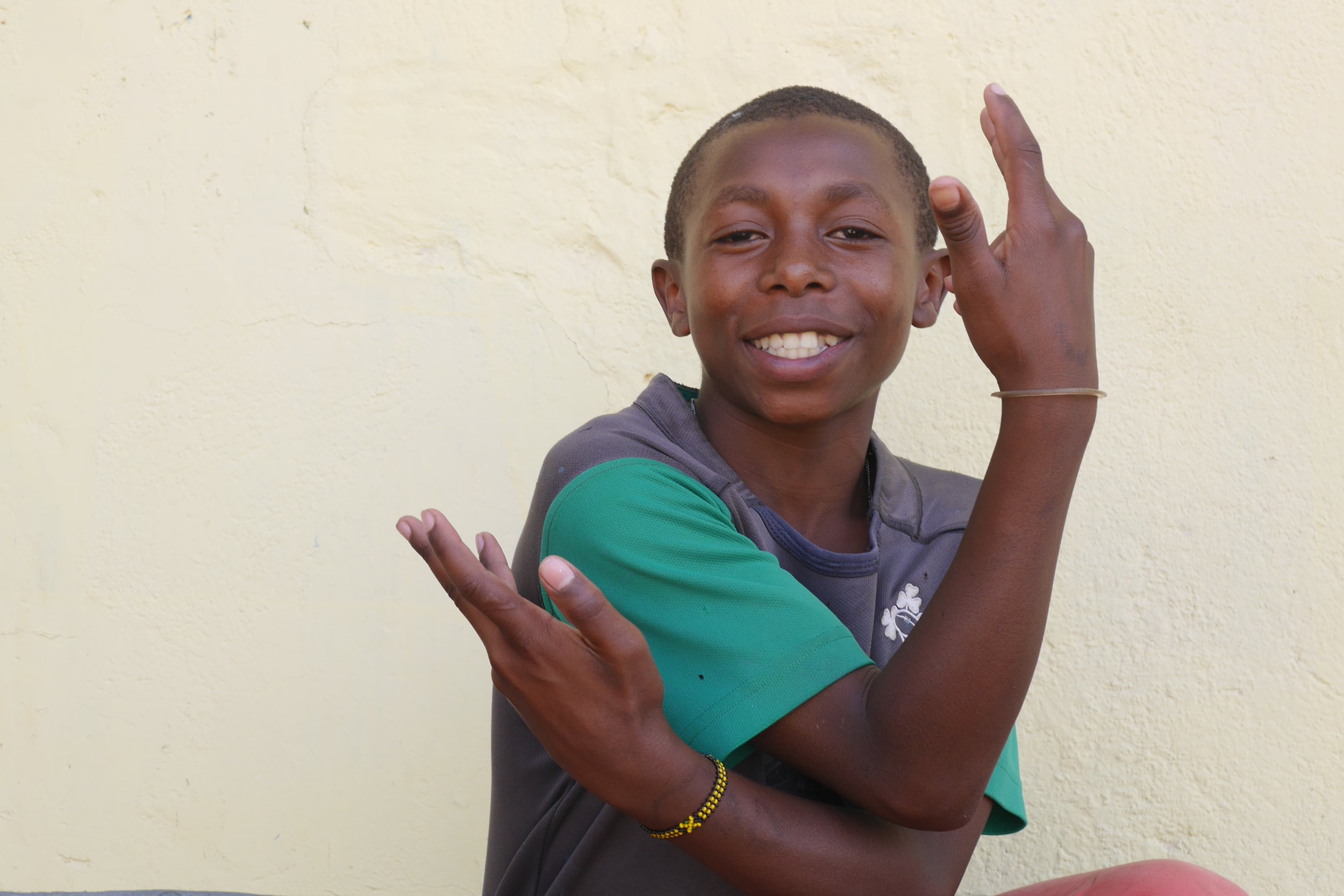 An older boy smiles toward the camera while raising their hands in a playful gesture.