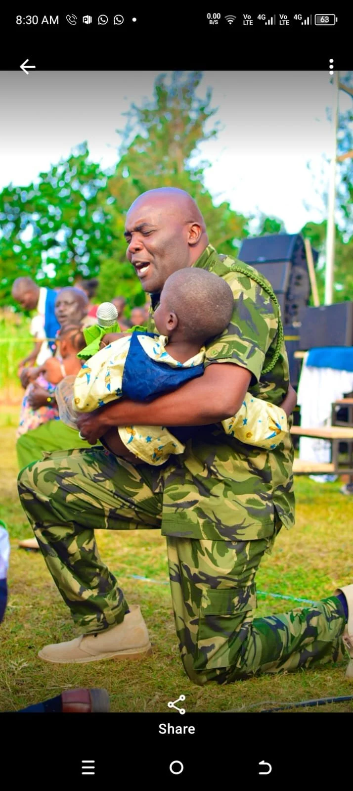 A man holds a child while speaking into a microphone outdoors.