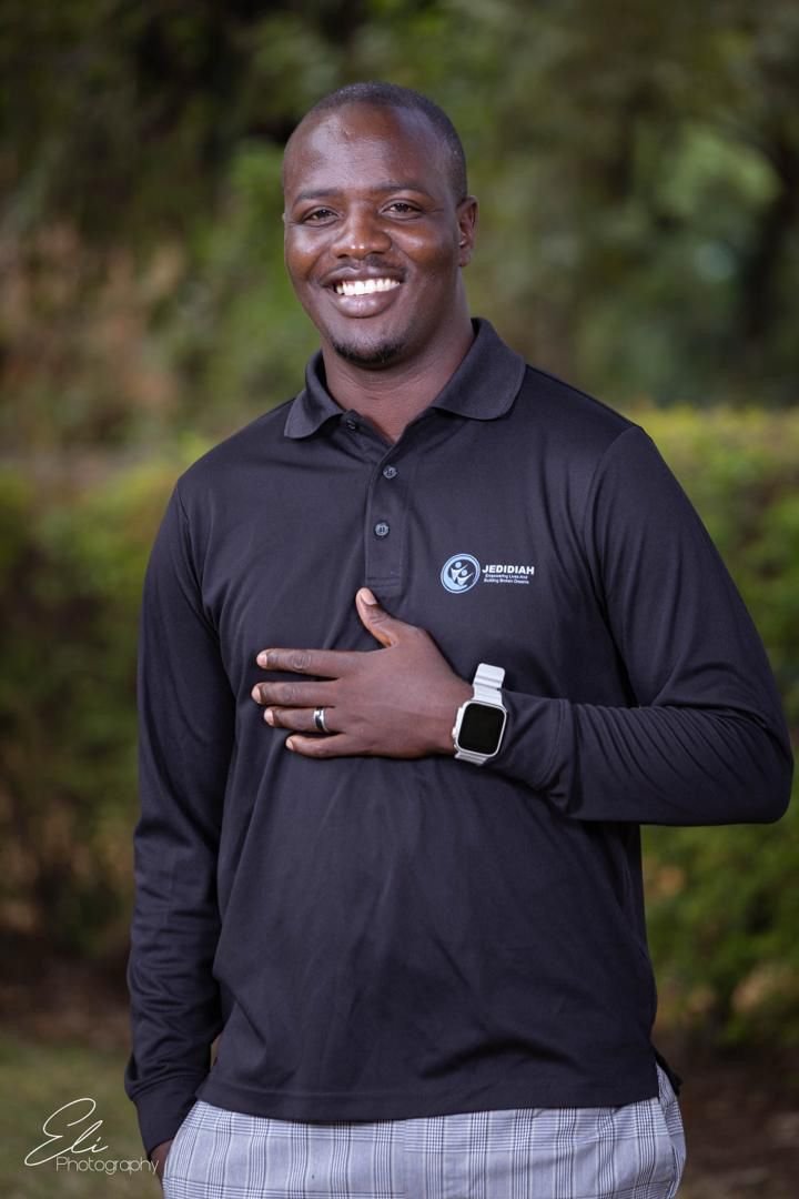 A man smiles toward the camera with one hand resting on his chest.