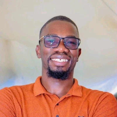 A man wearing glasses and an orange shirt smiles toward the camera.