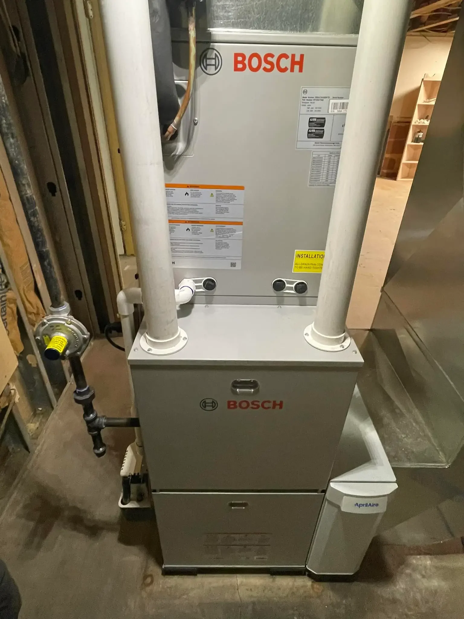 A Bosch HVAC unit, installed in a basement or utility room, with pipes and ducts connected to it.