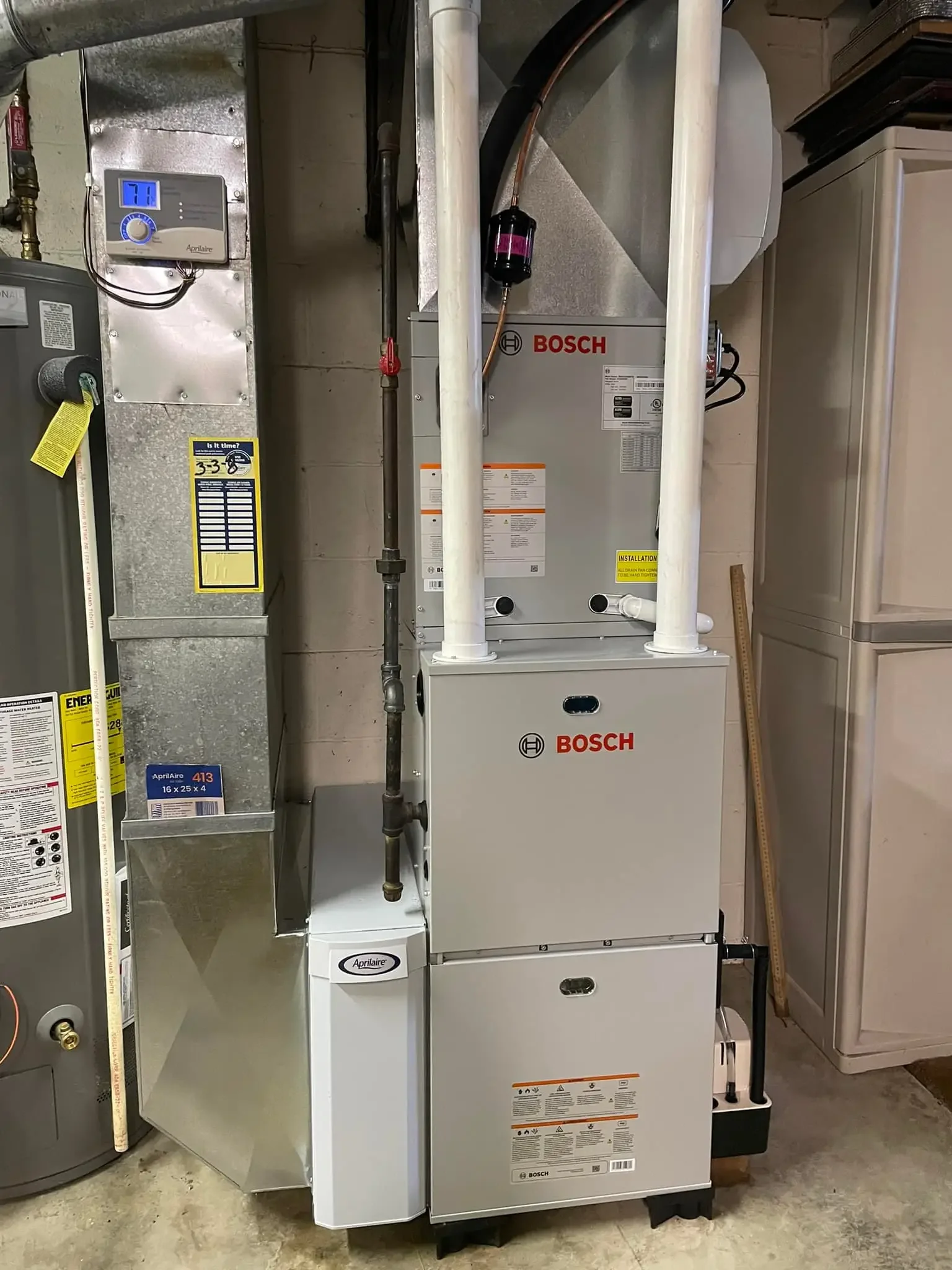 A Bosch furnace or HVAC system installed against a wall in a utility room, with a digital thermostat above it