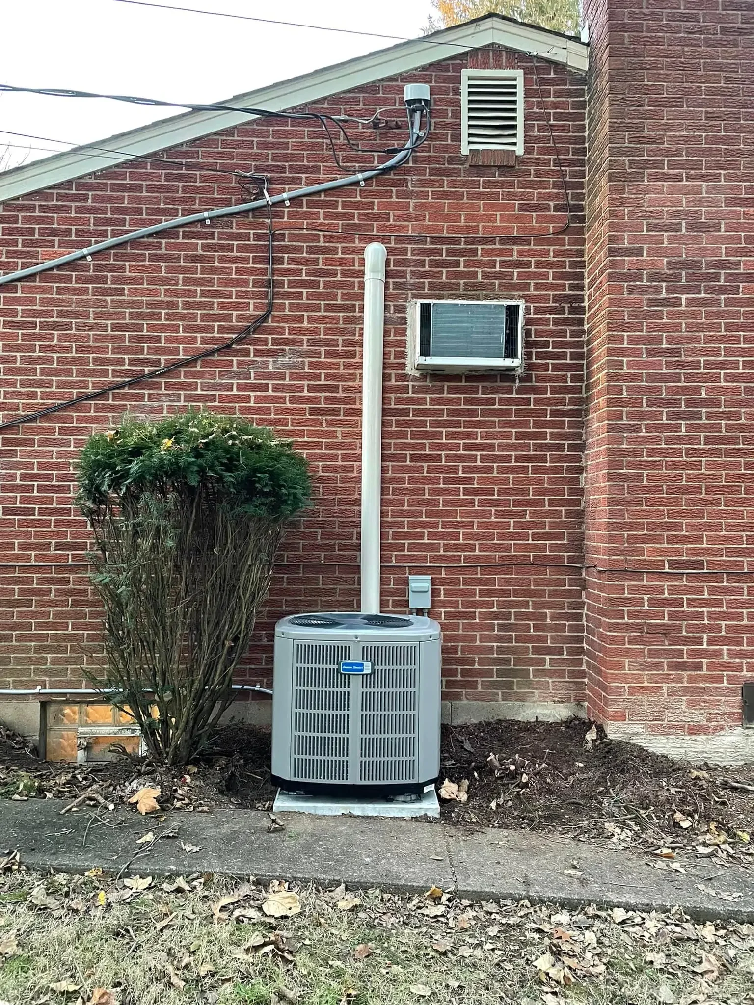 Backyard with a brick house wall, a bush, an air conditioning unit, an outdoor electrical box, and some modules.