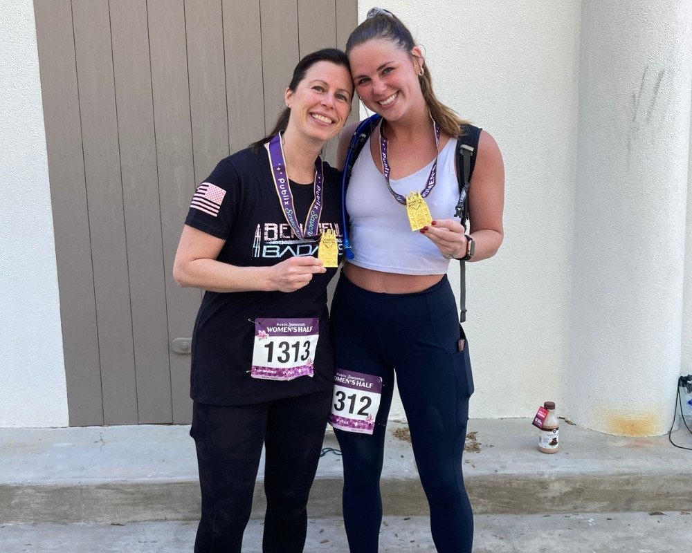 Two women with race bibs and medals, smiling and standing together after a race.