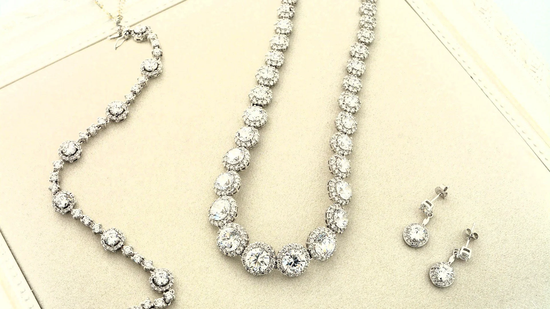 Set of diamond jewelry including a necklace, bracelet, and pair of earrings displayed on a beige surface.