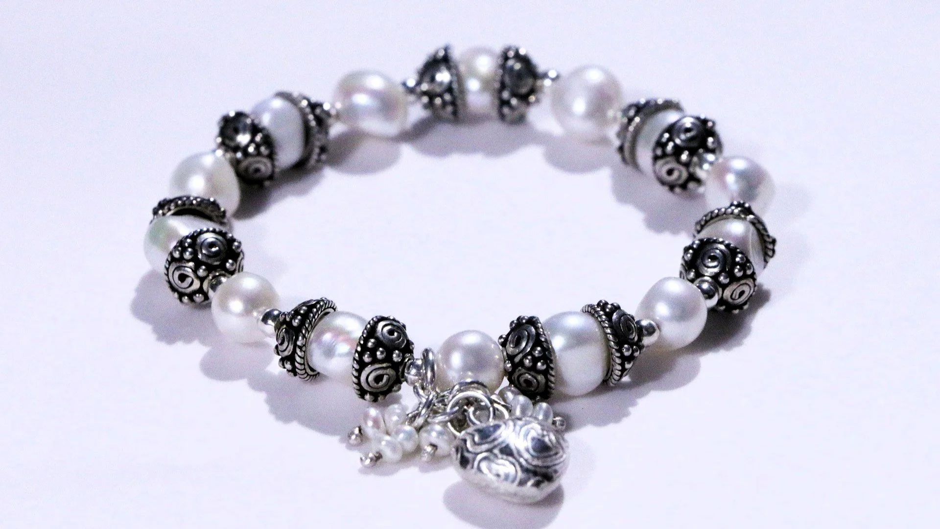 A pearl and silver charm bracelet with decorative beads and a heart-shaped charm.