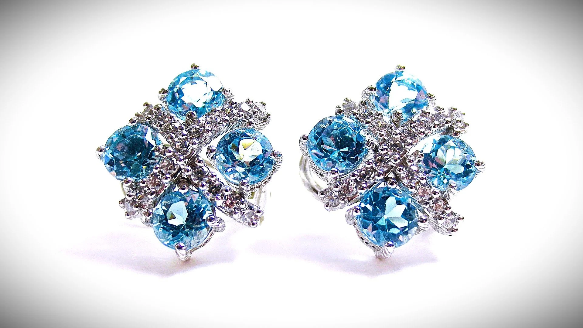 Pair of silver earrings decorated with multiple large blue gemstones and smaller clear rhinestones in a floral design.