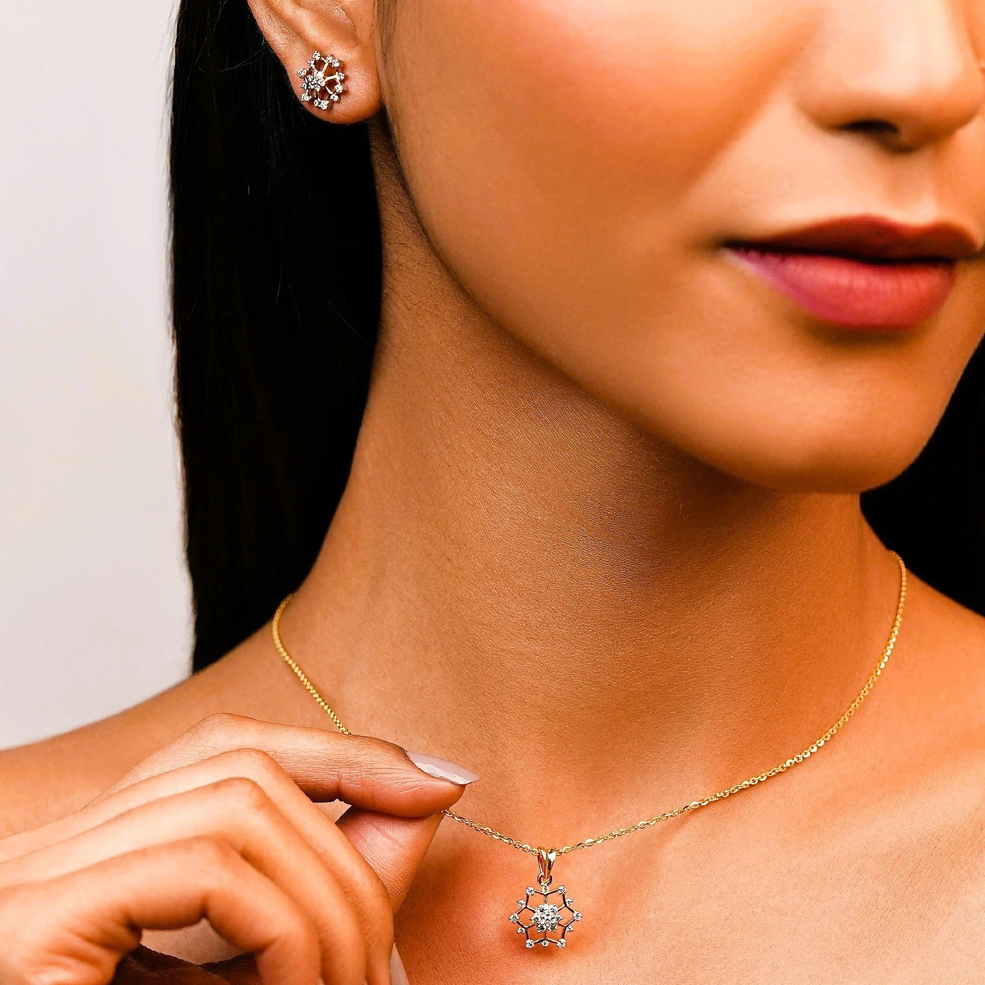 Close-up of a woman wearing a gold necklace with a snowflake-shaped pendant and matching earrings, touching her necklace.