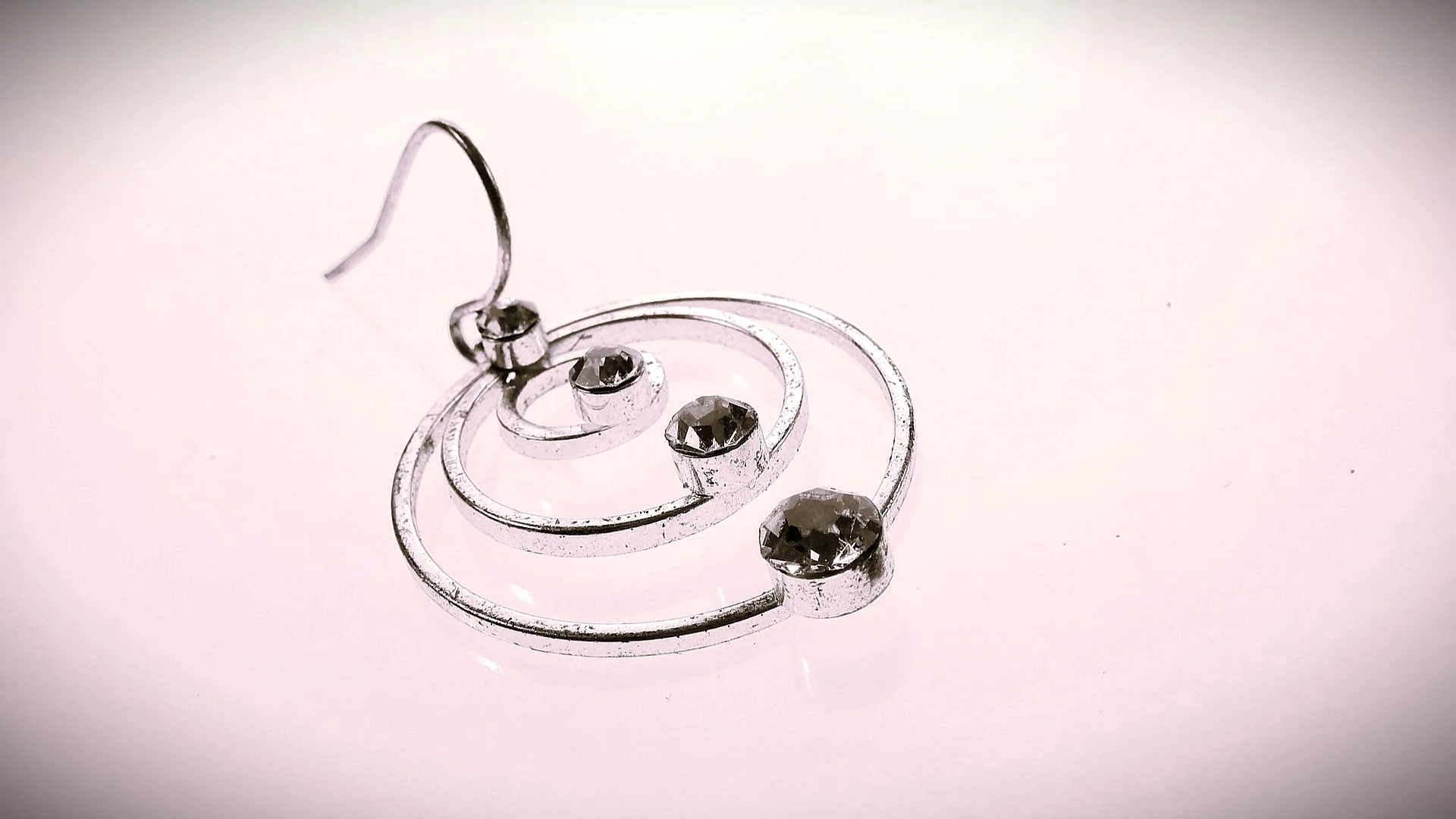 Silver earring with circular design and multiple black gemstones placed on a plain surface.