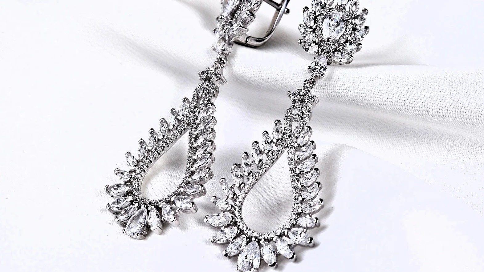 A pair of silver earrings with teardrop-shaped clear gemstones, resting on white fabric.