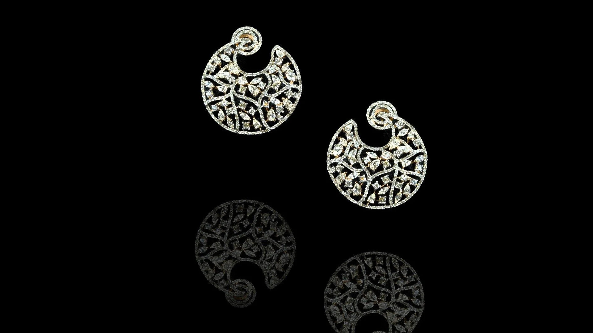 Pair of silver hoop earrings with intricate cut-out design, reflected on a black shiny surface.