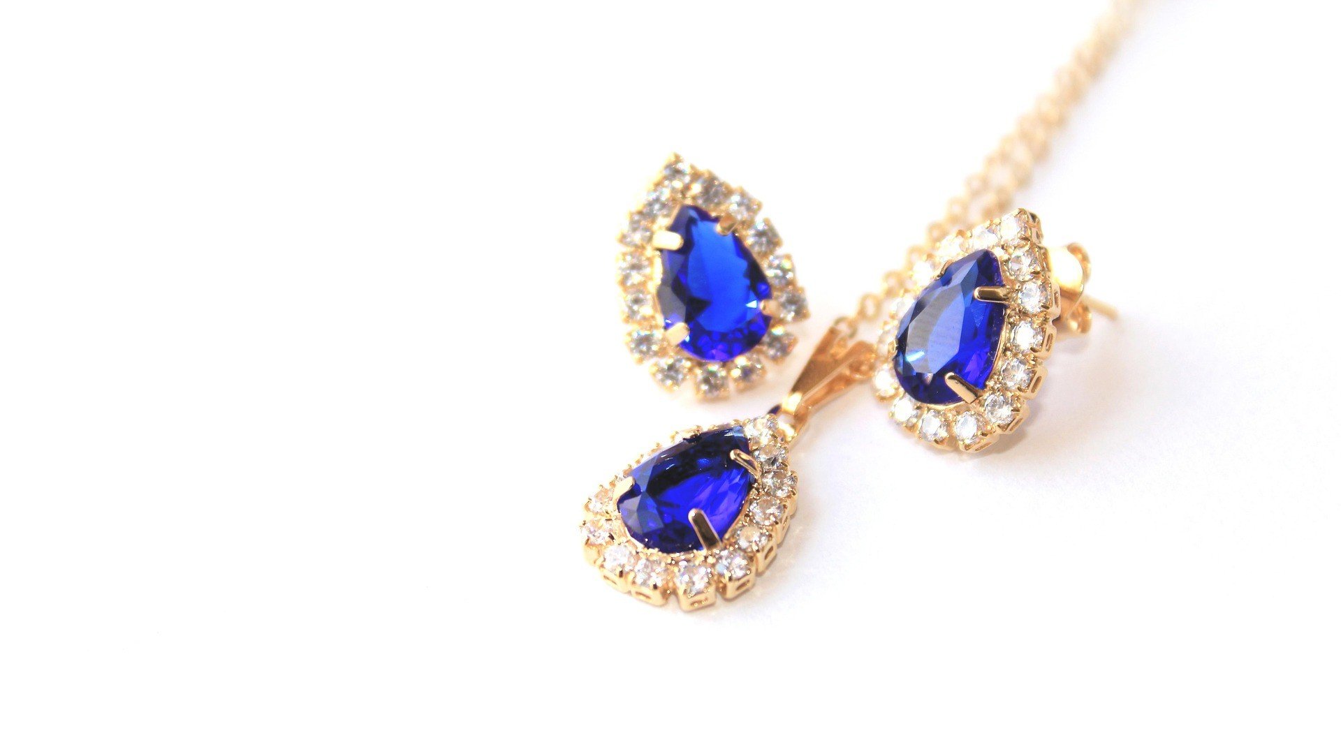 Gold jewelry set with large blue gemstones and surrounding small clear stones, including earrings and a pendant necklace.