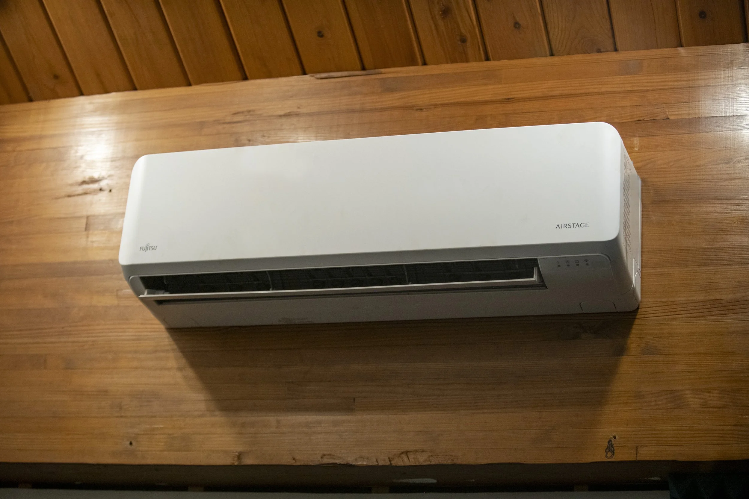 White Fujitsu air conditioning unit mounted on a wooden wall. Mini split unit.