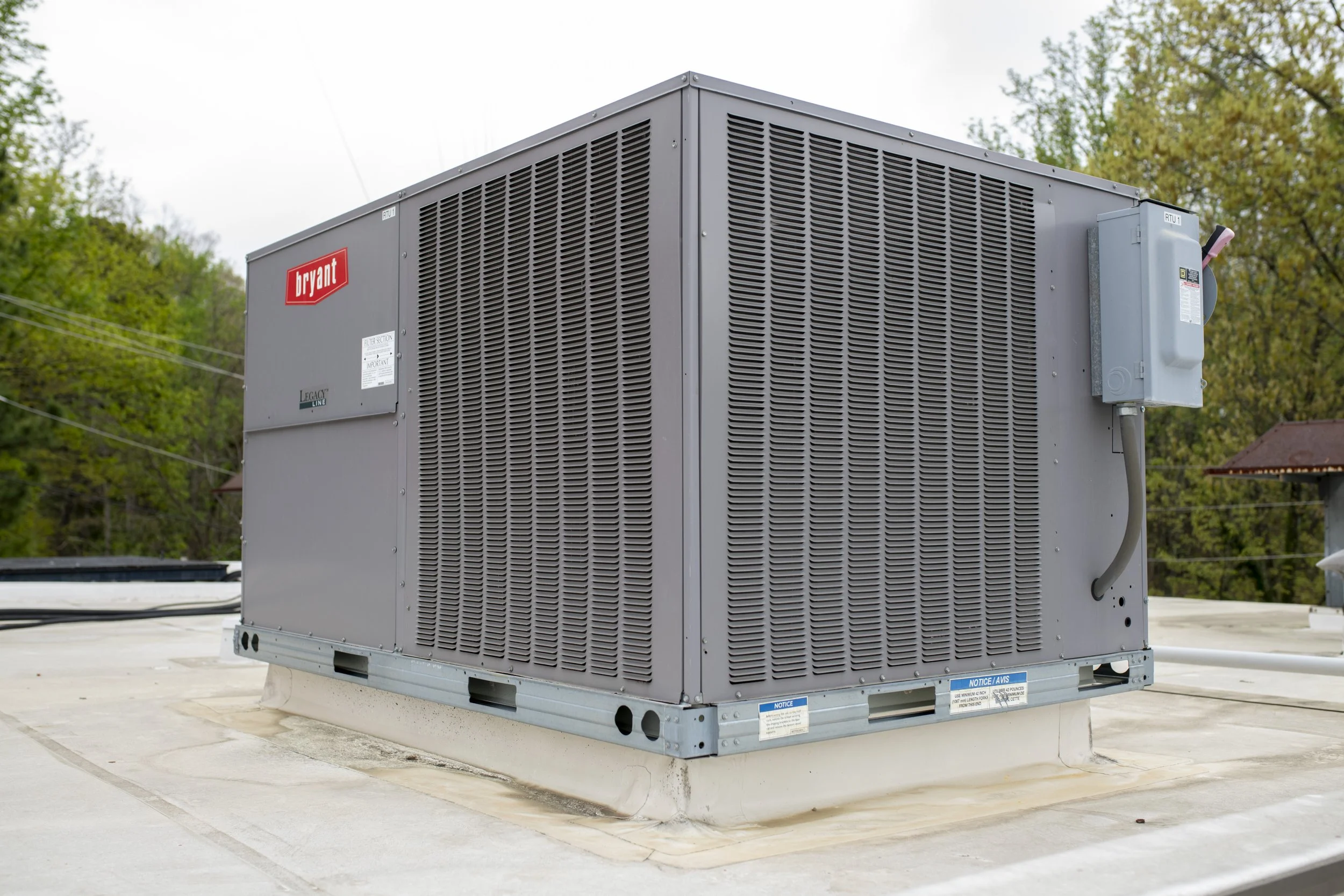 HVAC rooftop unit with gray metal panels, a red Bryant logo, and a small electrical box on the side, situated on a flat roof.