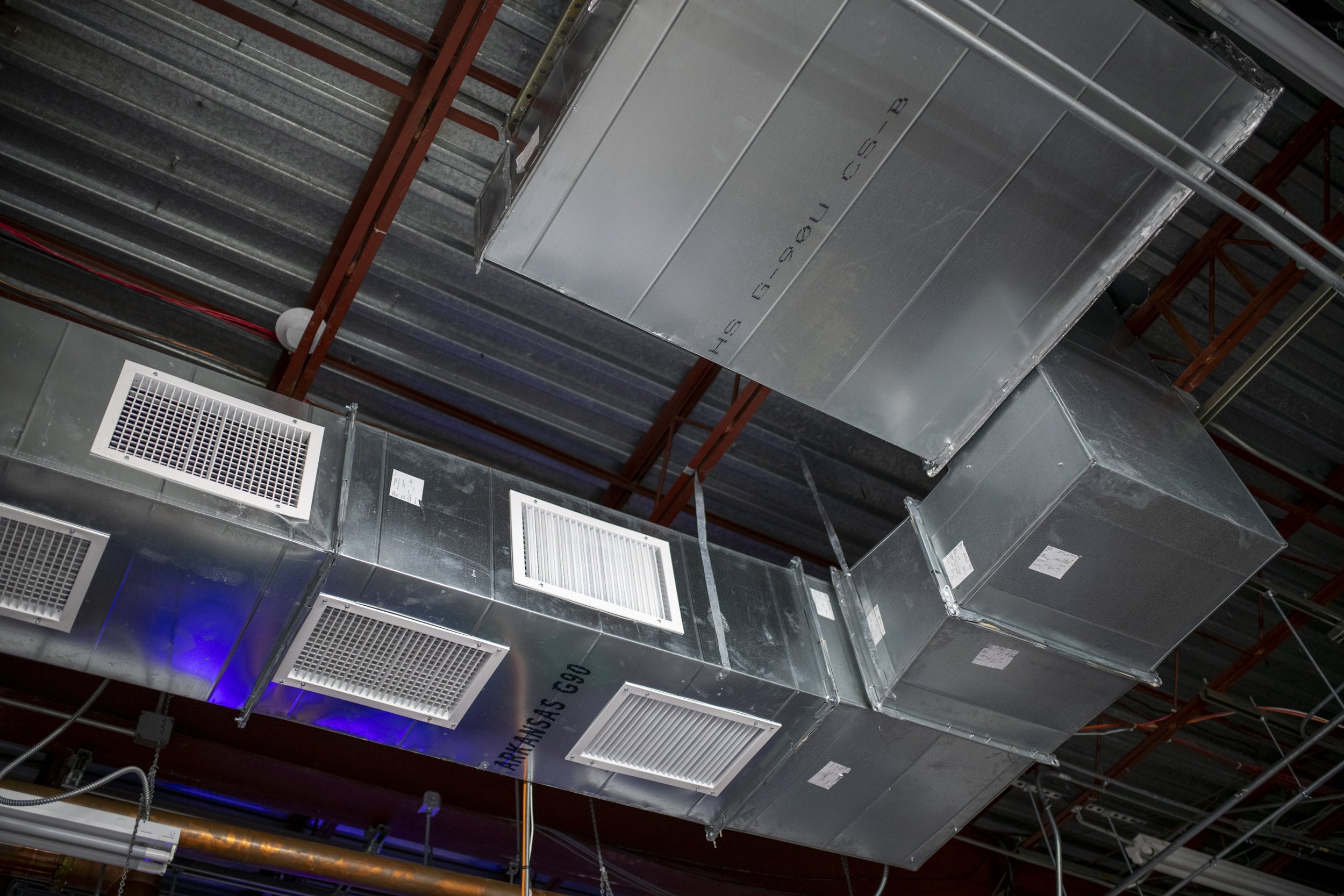 Industrial HVAC system components suspended from a ceiling, including rectangular ductwork with air vents and metal support structures.