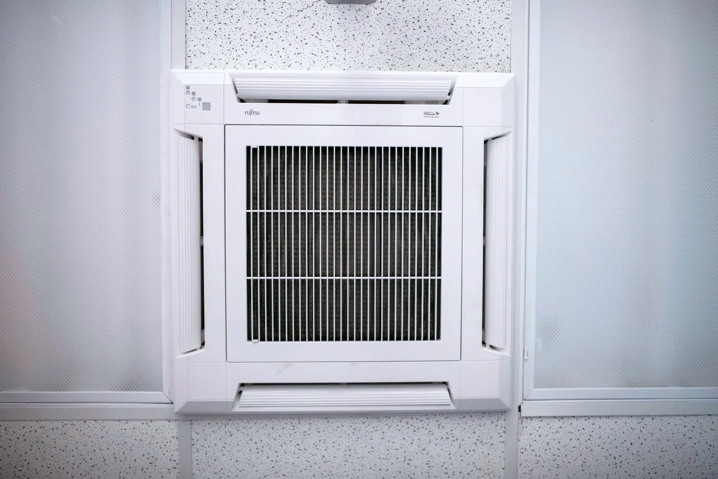 Ceiling air vent with white frame and black filter, installed in a white drop ceiling with perforated tiles.