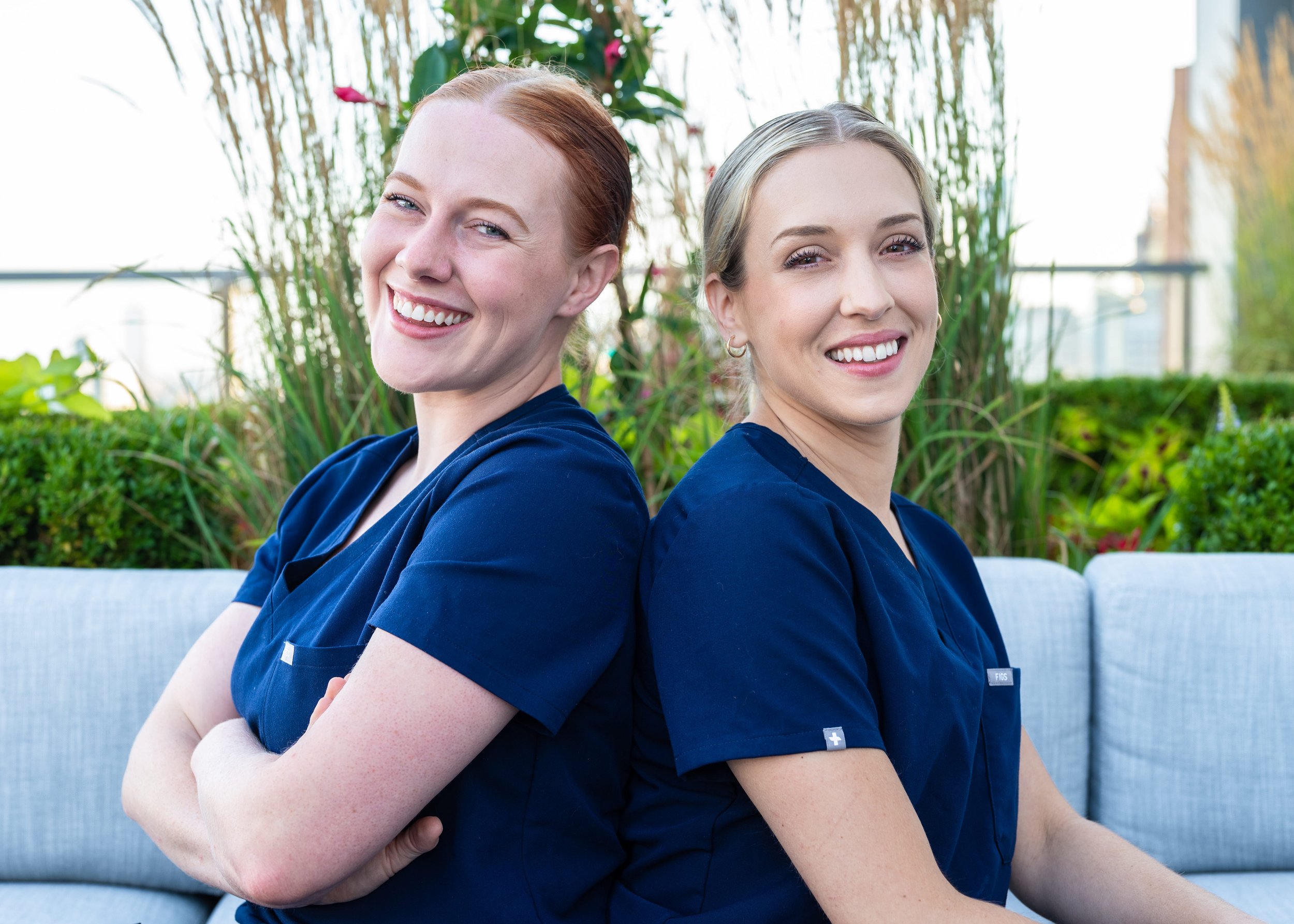 Anna Jobe, CRNA, and Chrissy Massaro, CRNA, founders of Confident Care Academy, sitting back-to-back and smiling.