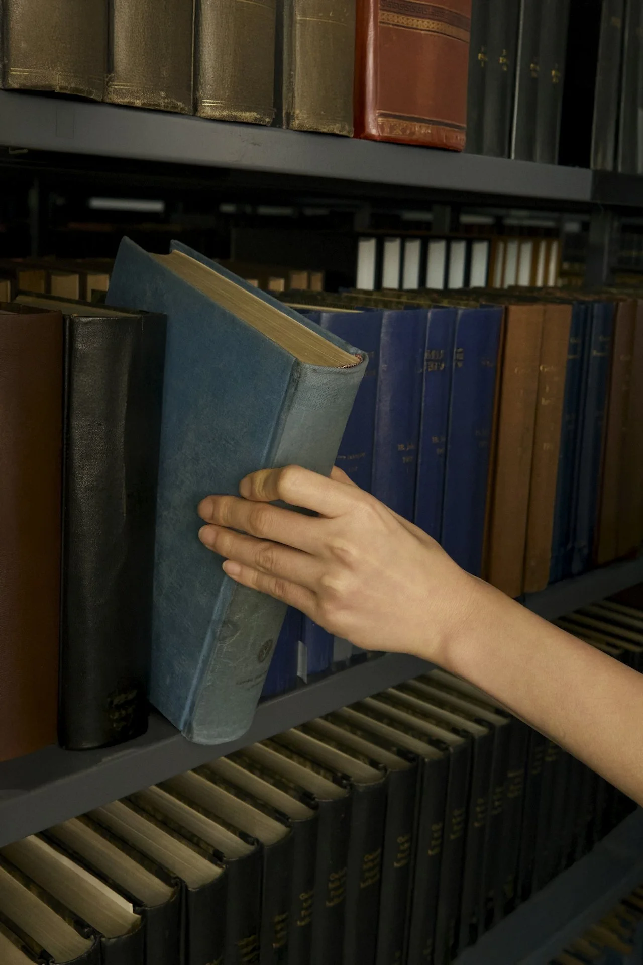 A hand pulls a reference book from a shelf, representing CCRN exam prep study resources from Confident Care Academy.