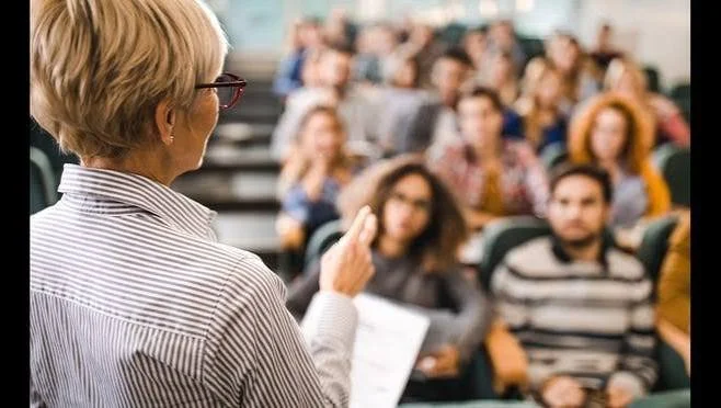 A woman giving a lecture or presentation to an audience in a lecture hall.